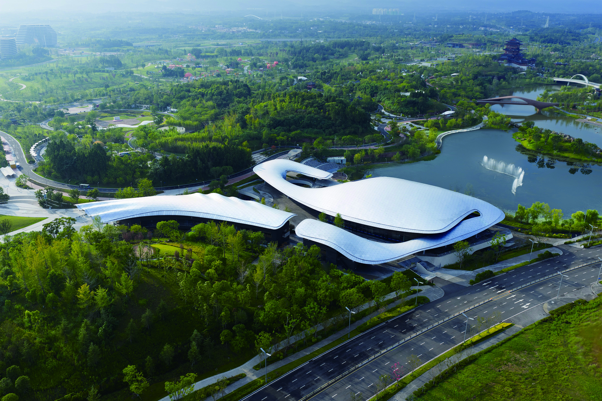 Aerial view of the undulating white roof nestled between dense green forest and a lake