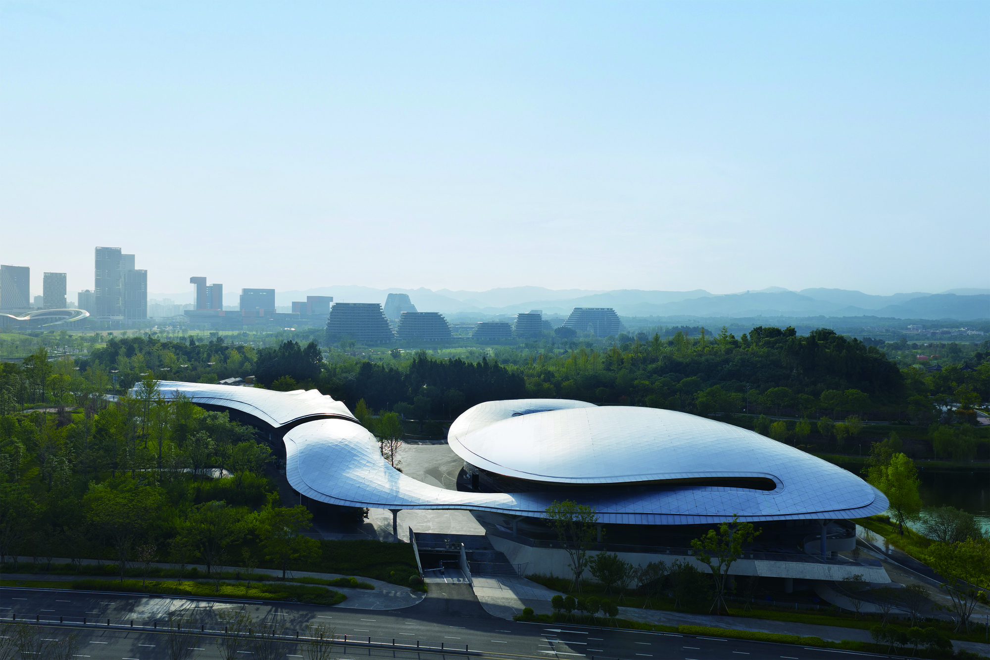 Elevated perspective showing the curved roof volumes against a backdrop of distant mountains and haze