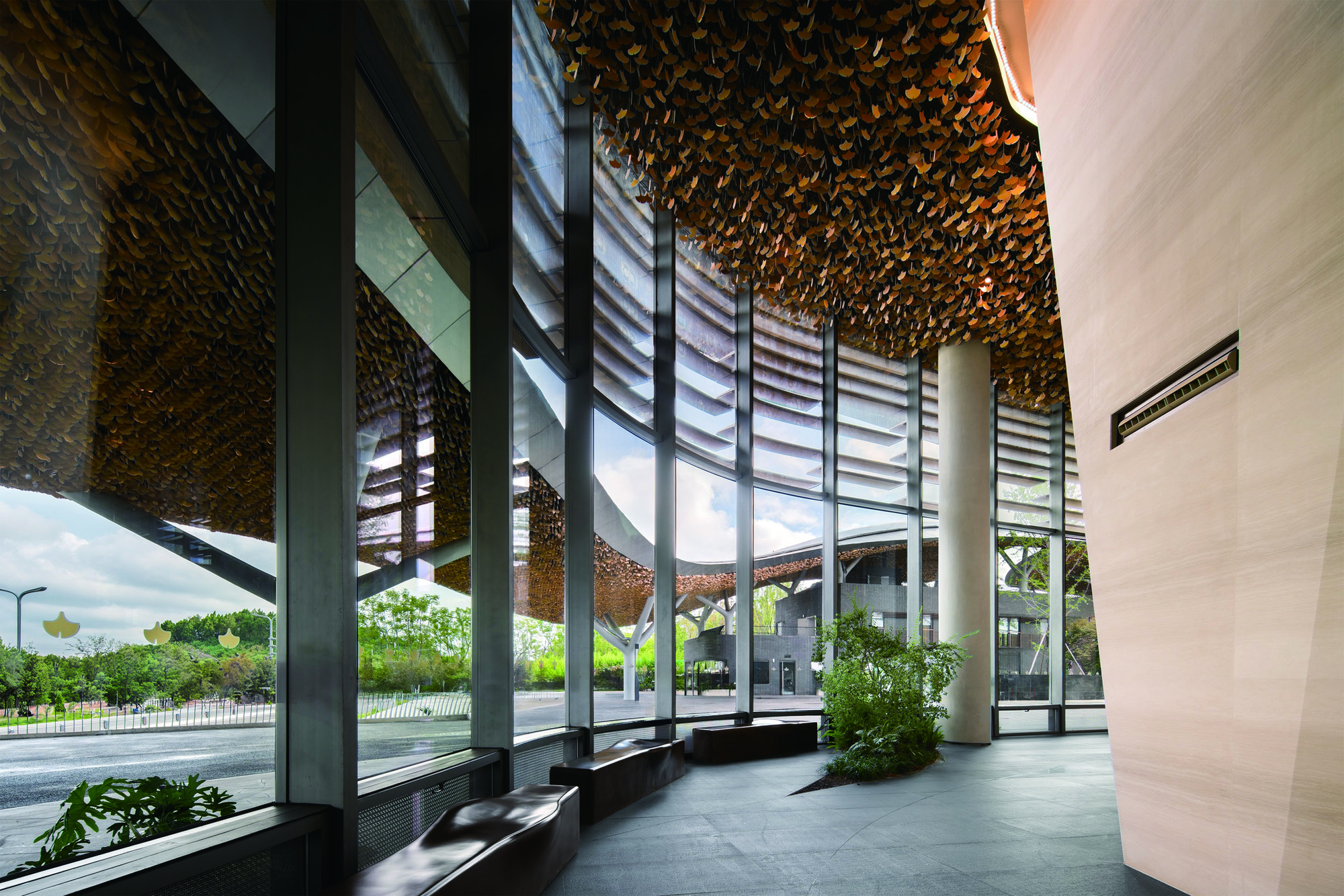 Interior lobby with glass curtain walls, louvered screens, and golden ceiling beneath the canopy