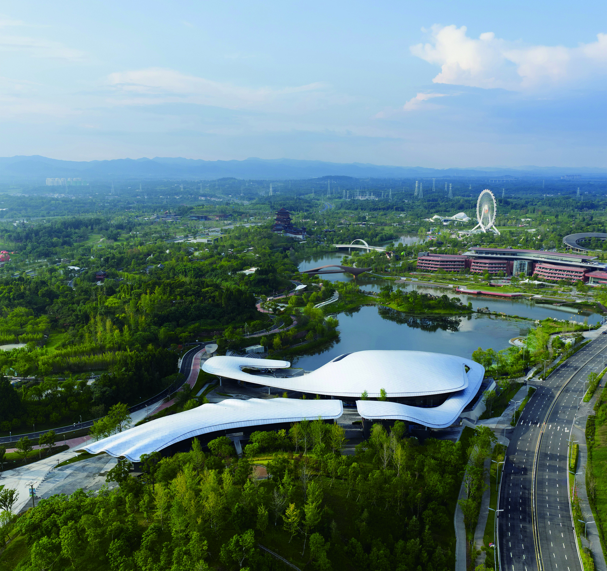 Aerial view of the curved white roof surrounded by parkland and waterways under afternoon clouds