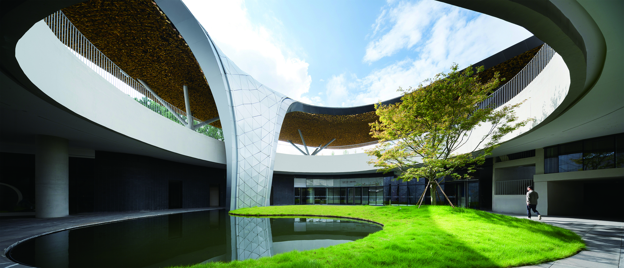 Interior courtyard with circular reflecting pool, lawn, and curved roof canopy overhead with planted soffit