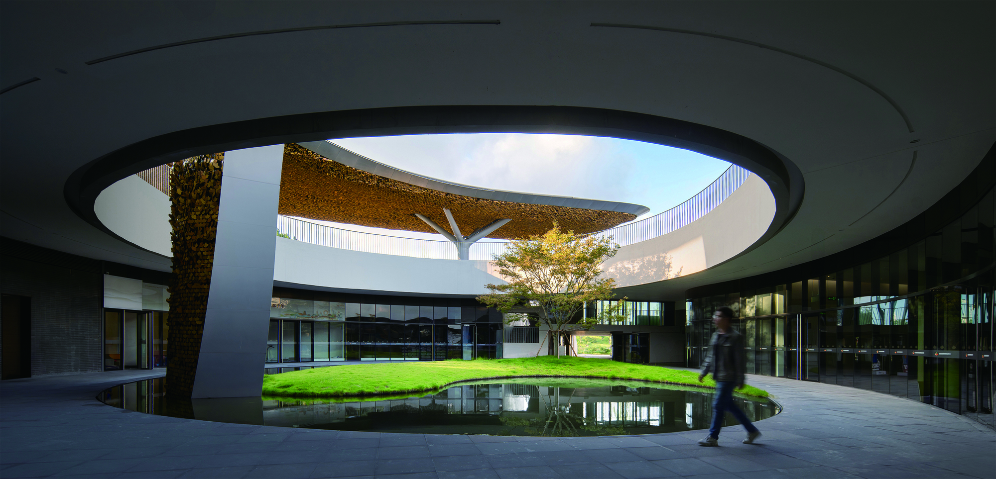 Circular oculus framing the central courtyard as a figure walks beneath the cantilevered roof edge