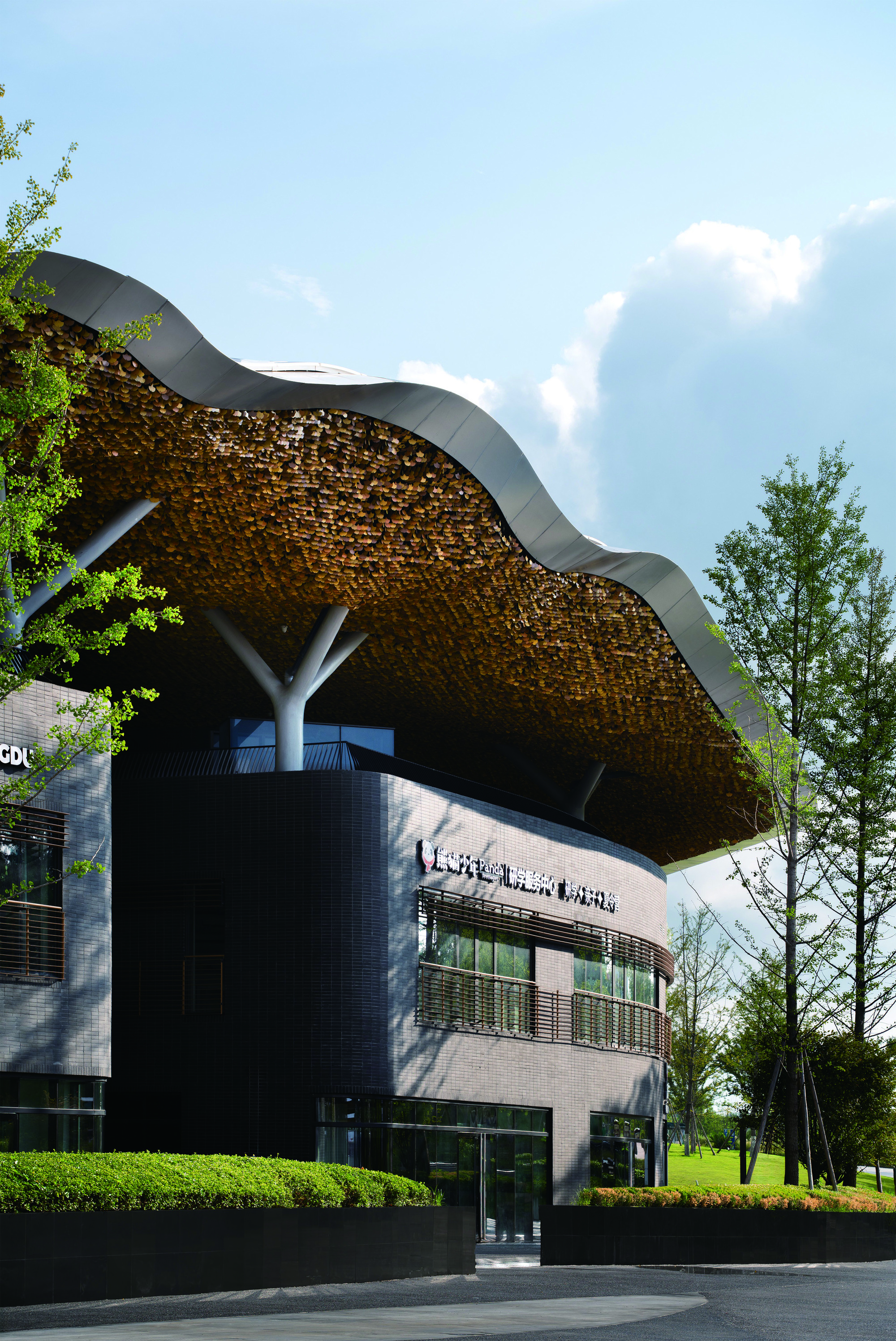 Street view of the woven roof canopy over a dark tile facade with young trees