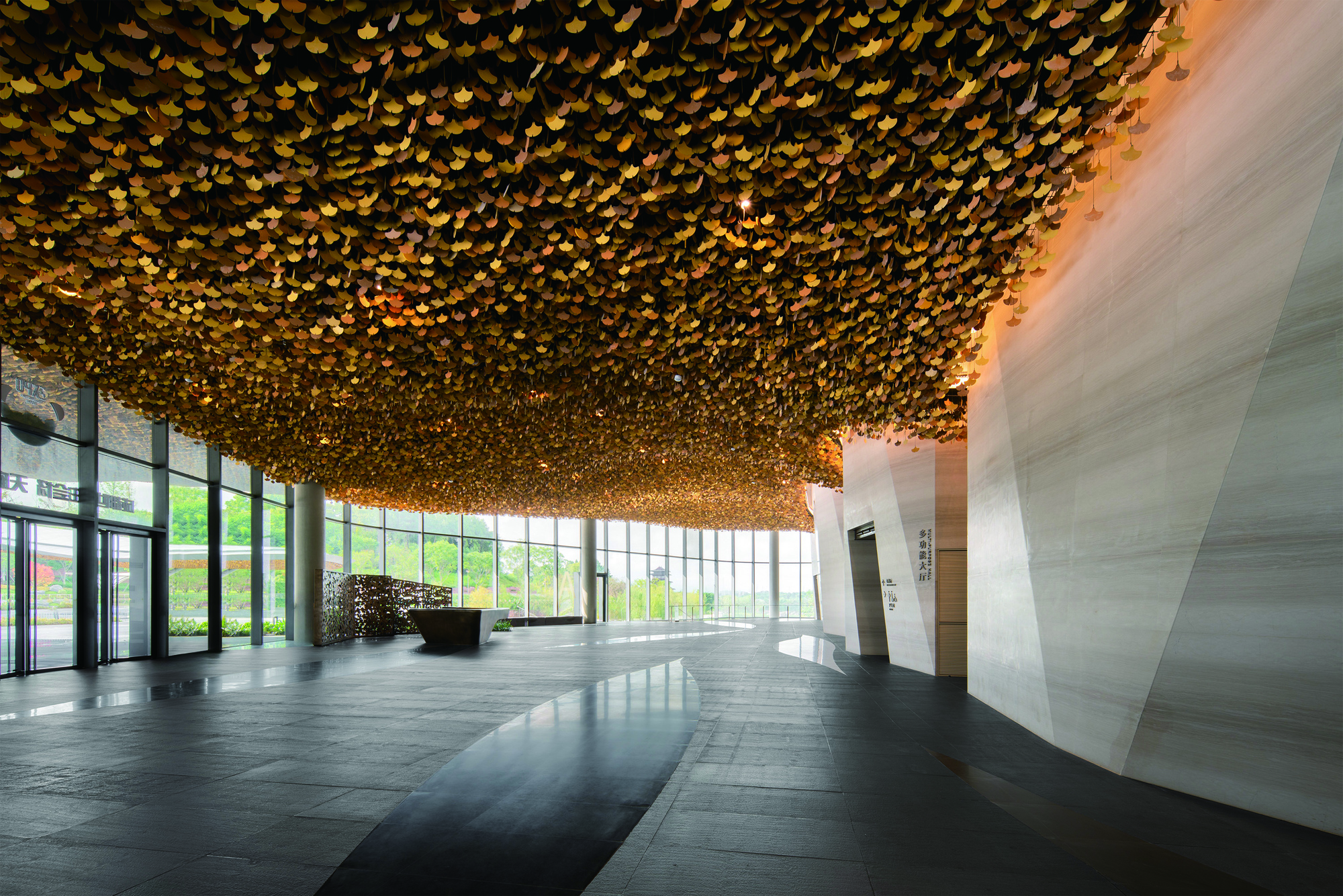 Interior lobby with textured golden ceiling installation above dark stone floors and white angled walls