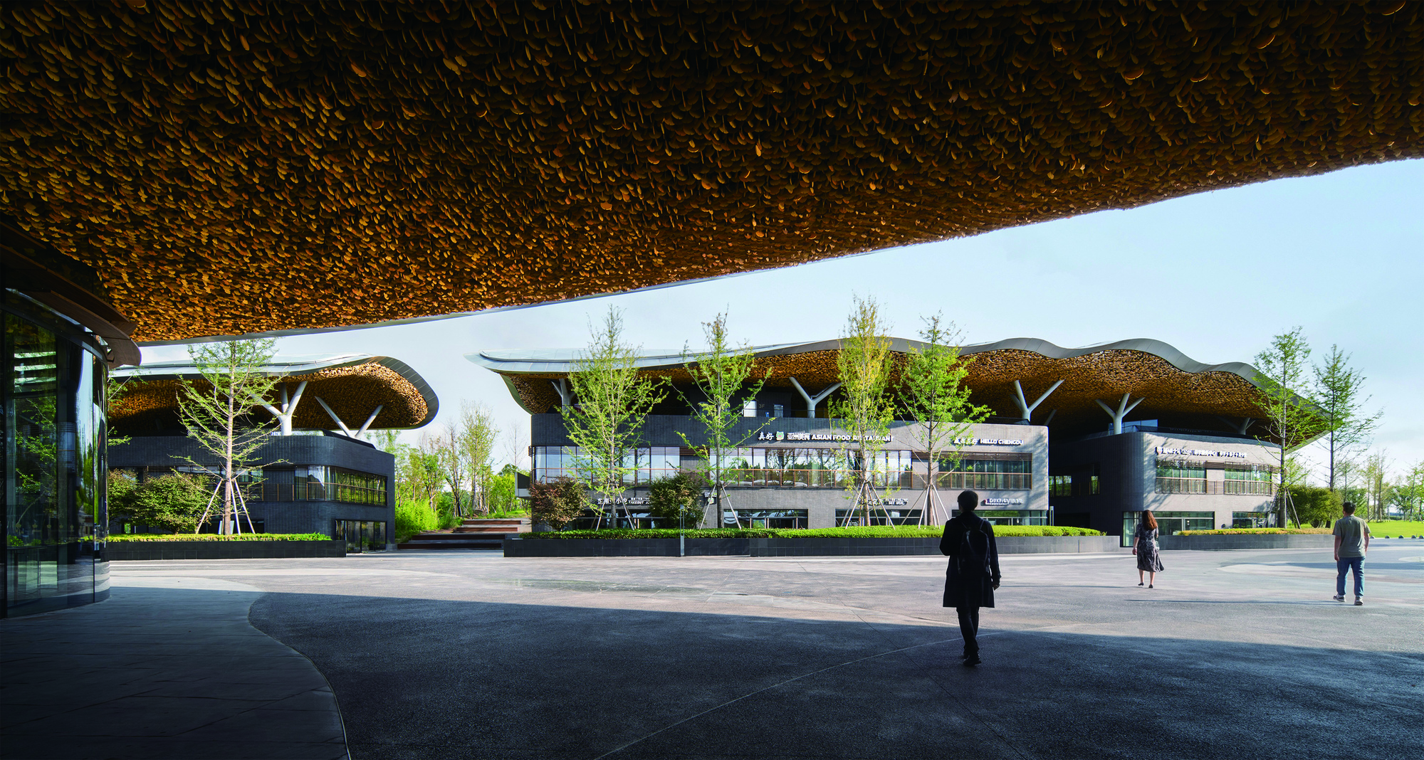 Plaza view showing multiple undulating roof canopies supported by white branching columns with pedestrians crossing
