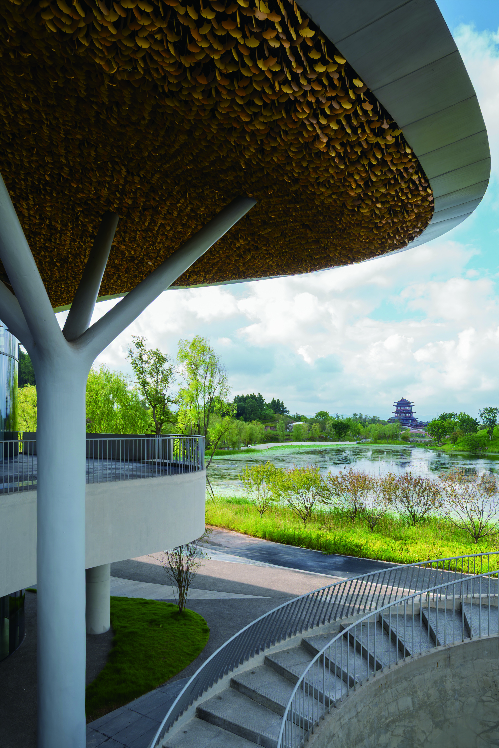 Exterior terrace under the scalloped roof edge overlooking a wetland and distant pagoda