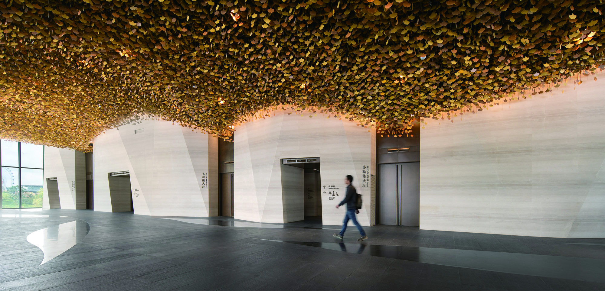 Elevator lobby with textured golden ceiling and pale stone walls as a figure passes by