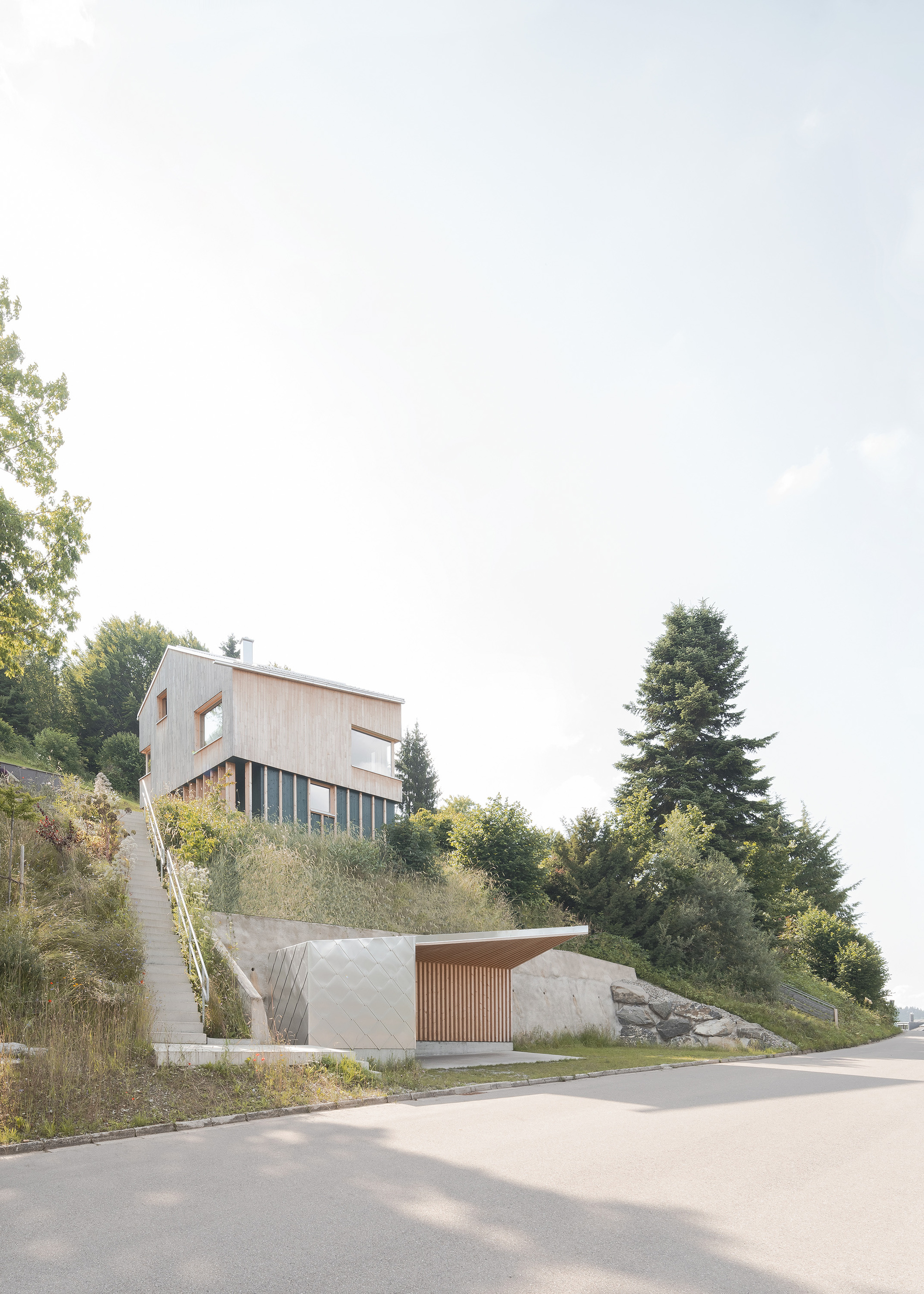 Hillside street view showing timber-clad upper volume on slats above concrete lower garage with slatted door