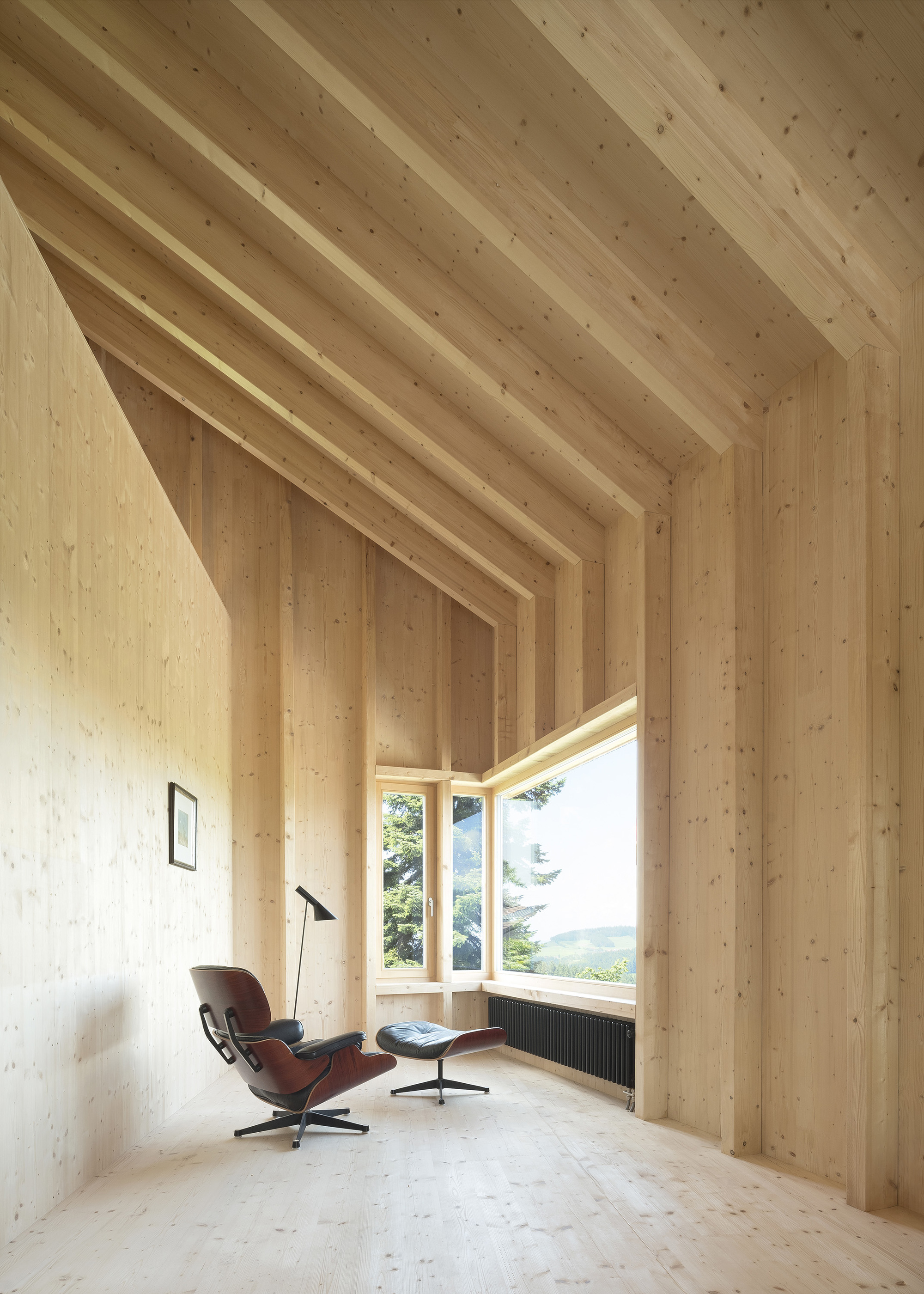 Interior view of exposed timber beam ceiling framing a corner window with lounge chair and floor lamp