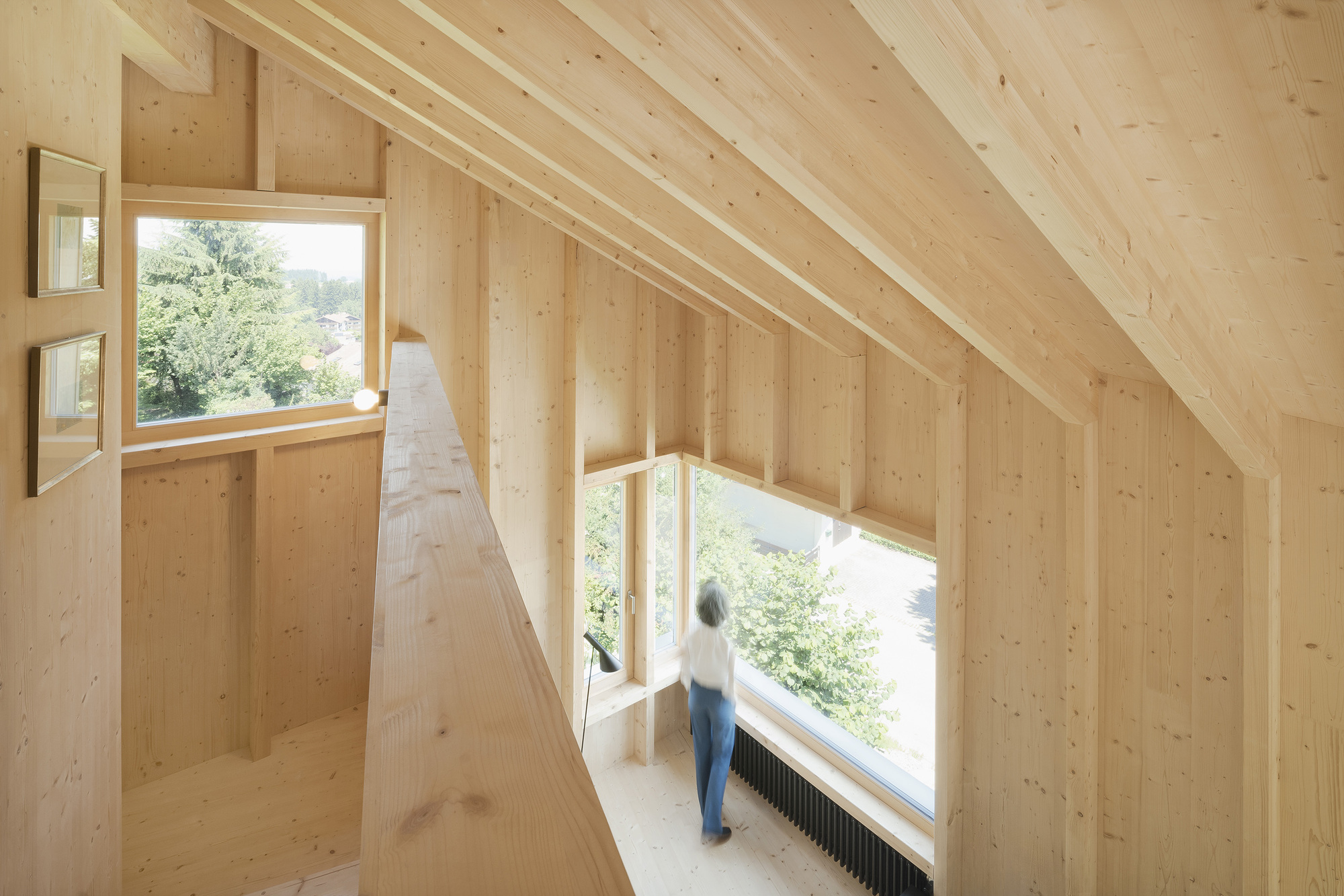 Upper-level interior hallway with exposed timber framing and person standing at window overlooking landscape