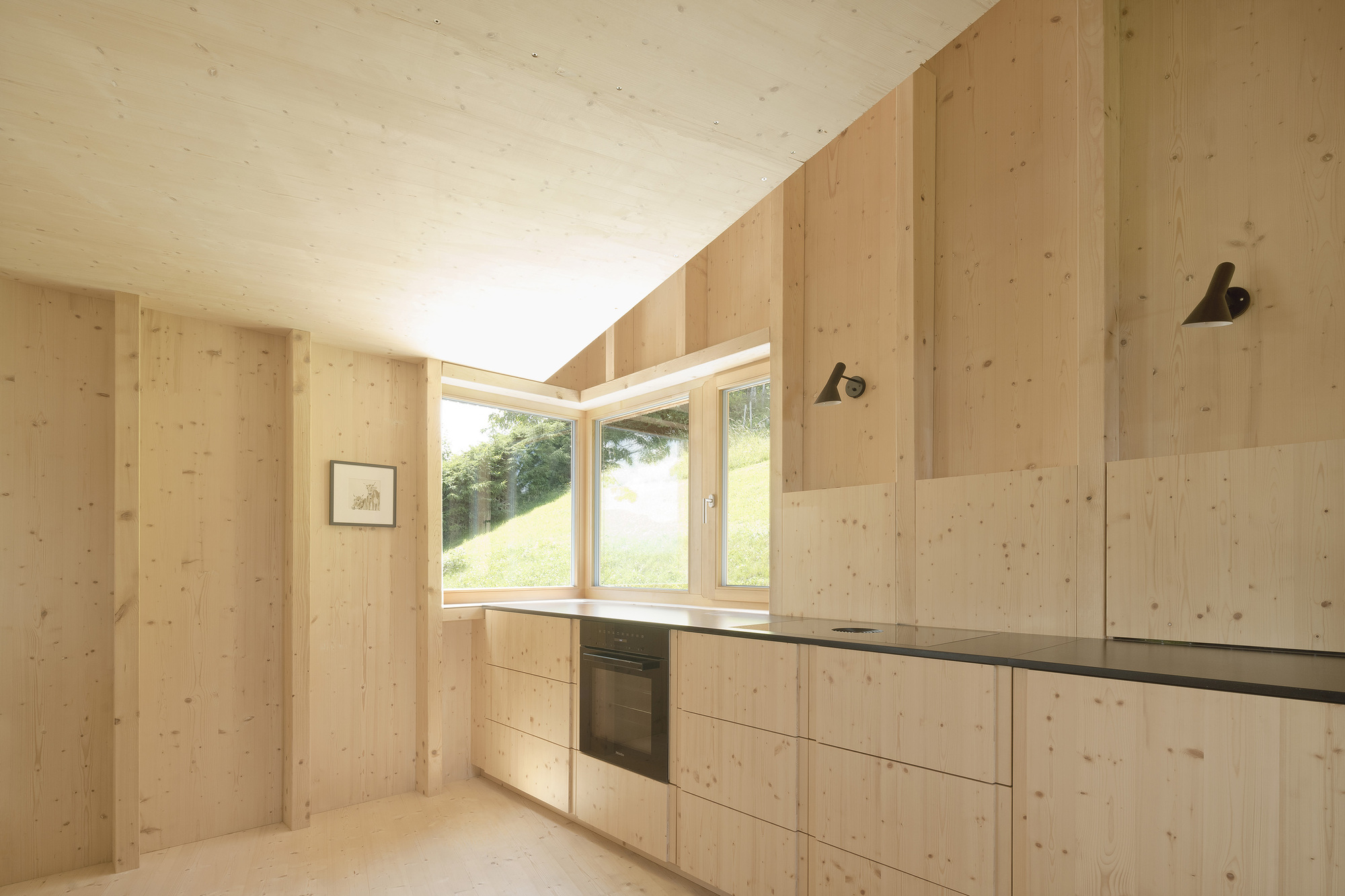 Kitchen interior with exposed timber walls and clerestory window framing view of grassy hillside