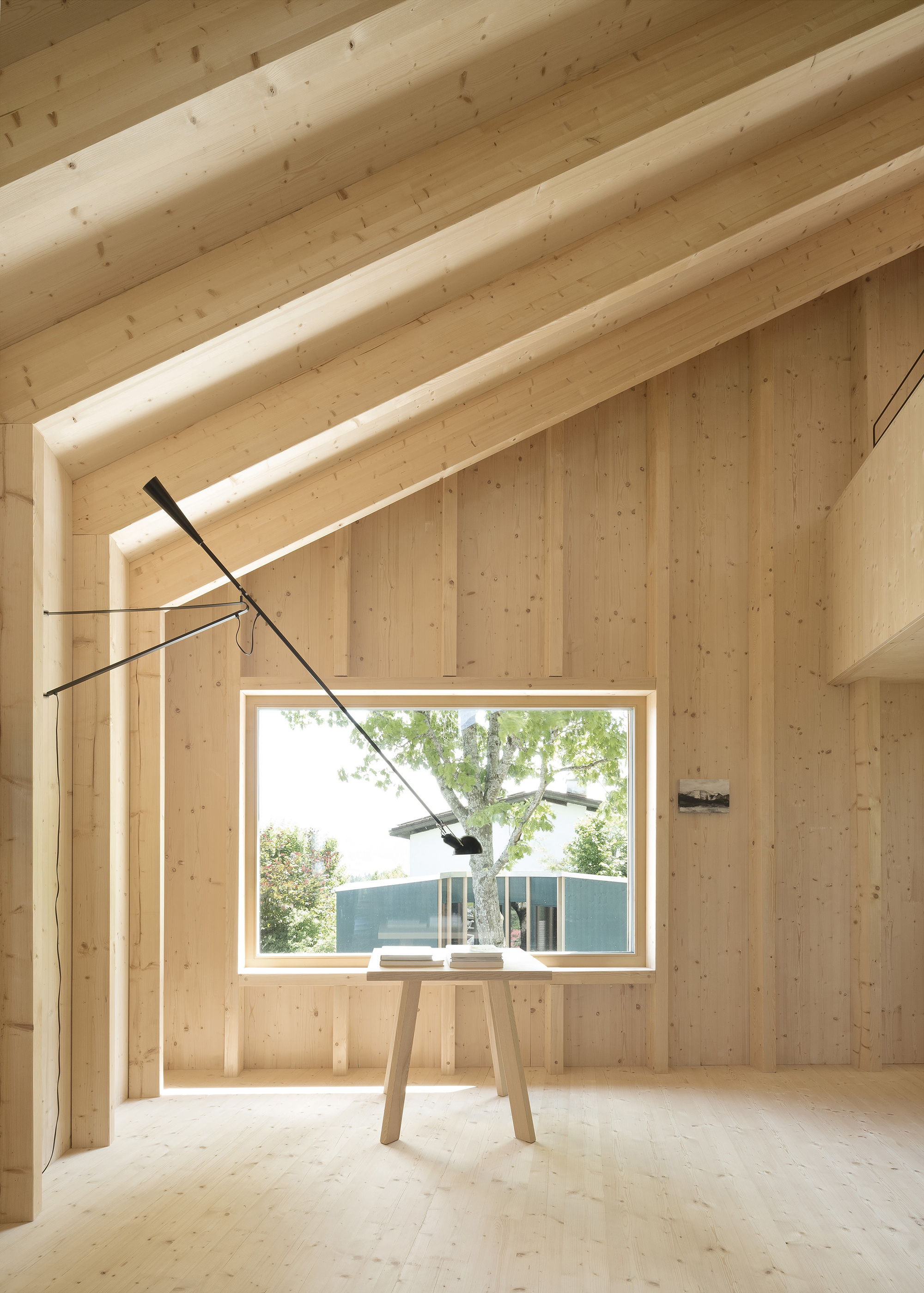 Double-height timber-lined room with picture window framing blue pavilion and cantilevered black pendant fixture