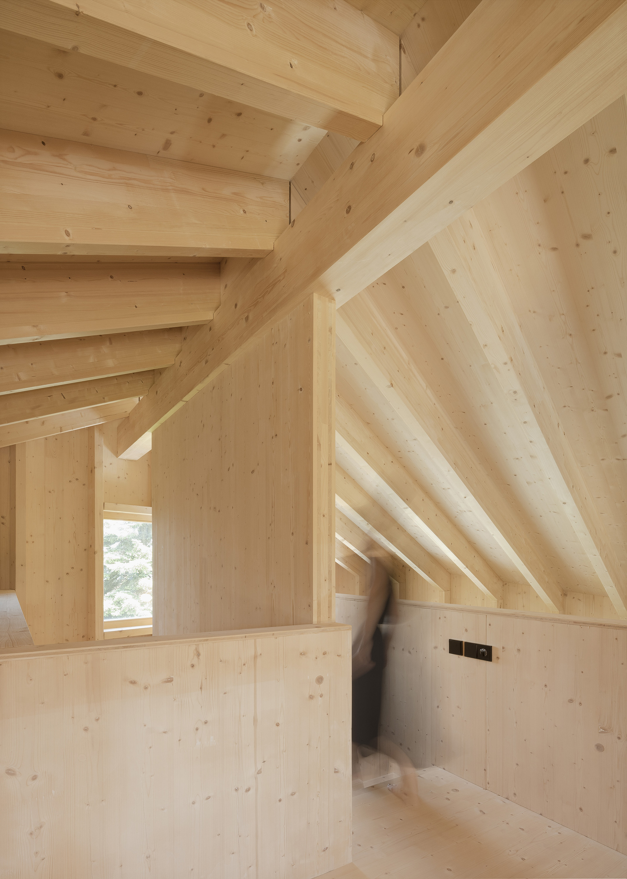 Interior room with exposed timber rafters and light wood walls with a blurred figure walking