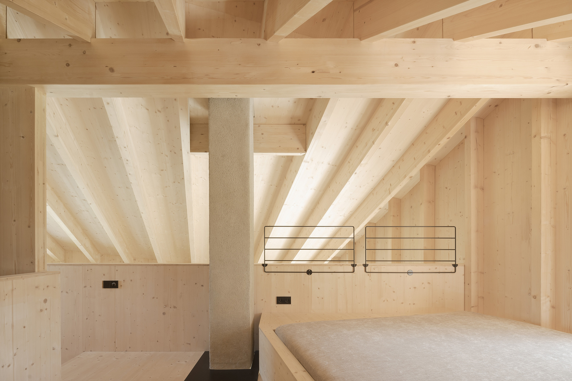 Bedroom with exposed timber beams, light wood walls and minimal steel frame bedside fixtures