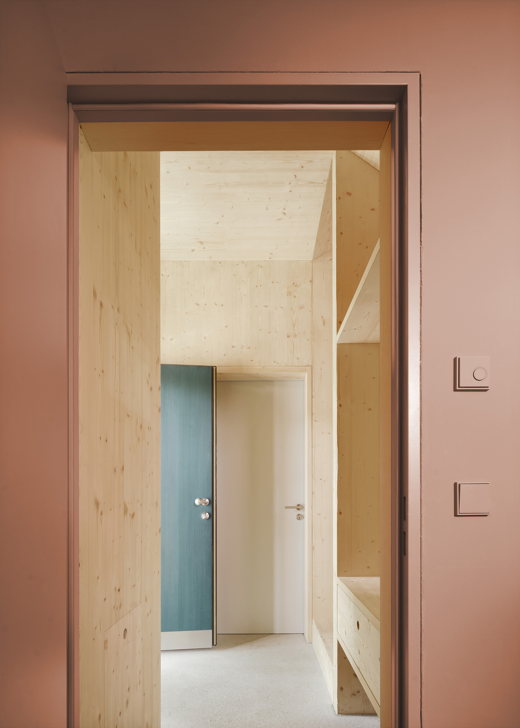 Doorway in a pink wall opening to a light wood corridor with blue and white doors