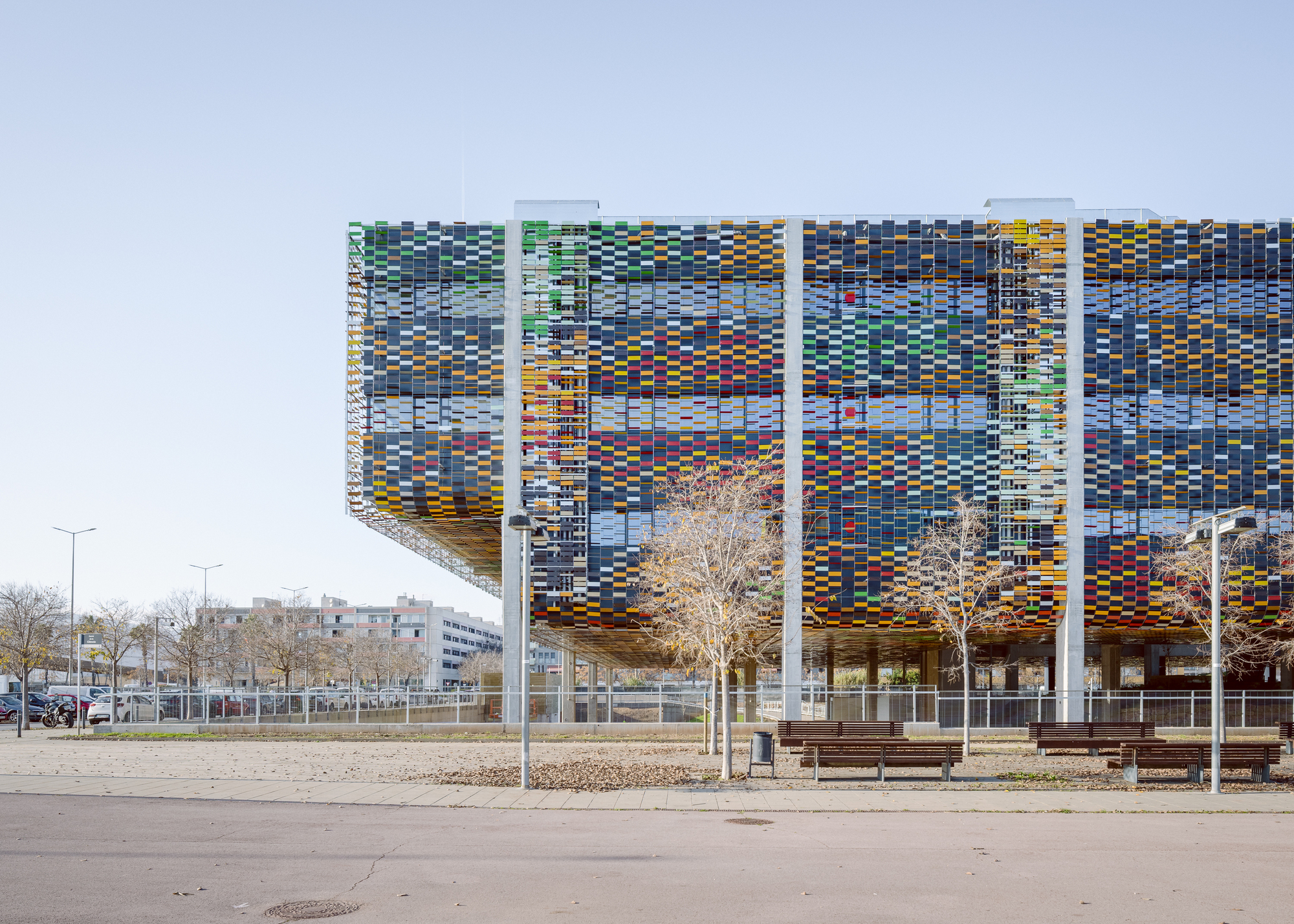 Long facade showing the pixelated screen with white structural columns and bare winter trees in foreground