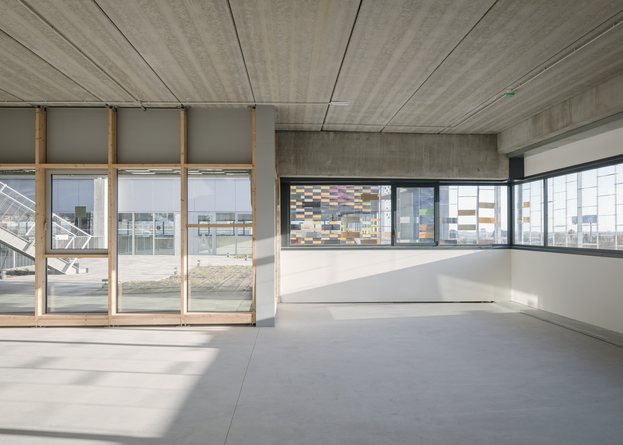 Interior space with board-formed concrete ceiling and floor-to-ceiling glazing overlooking the perforated ceramic facade