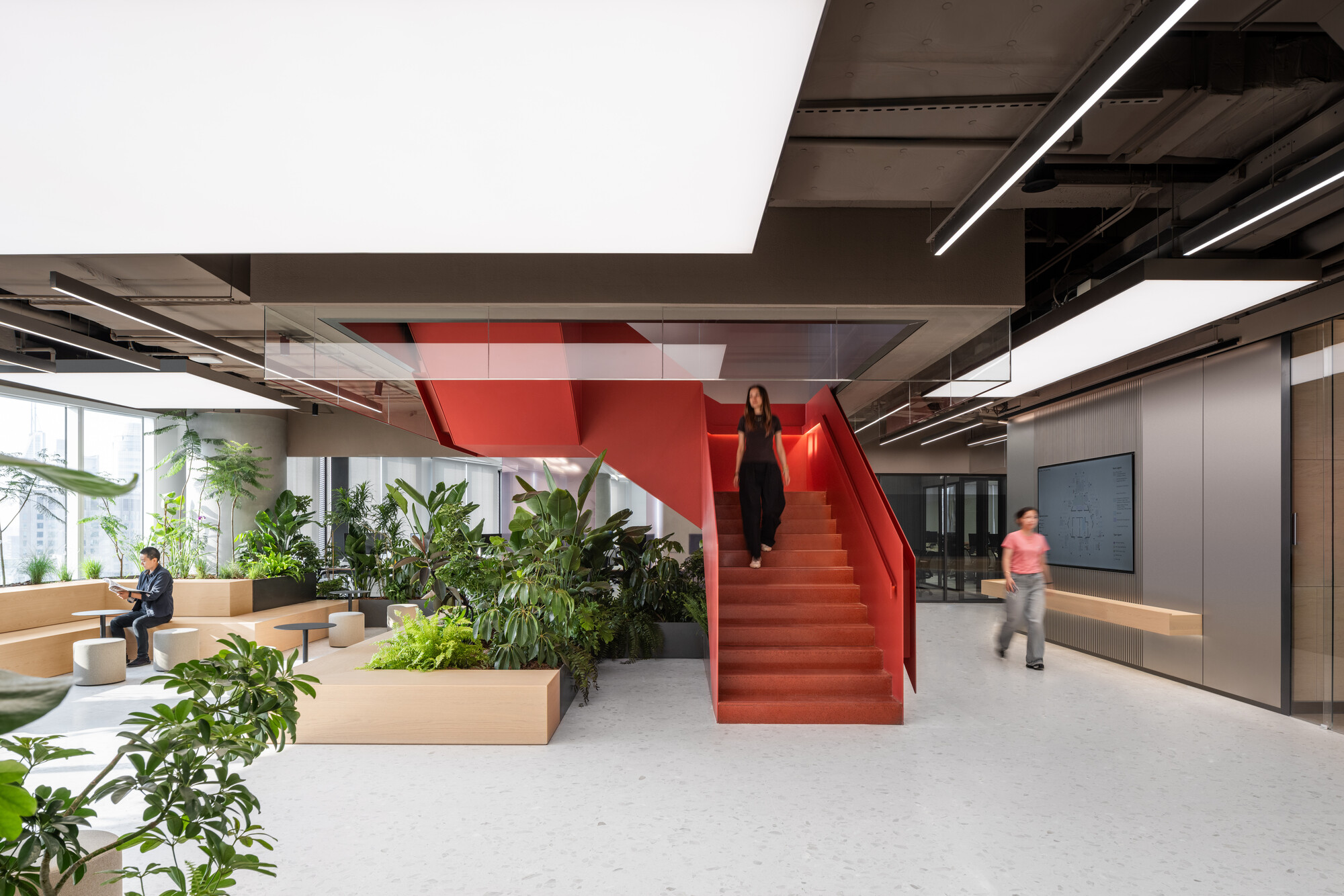 Red steel staircase rising through an office lobby with potted plants and exposed ceiling ducts