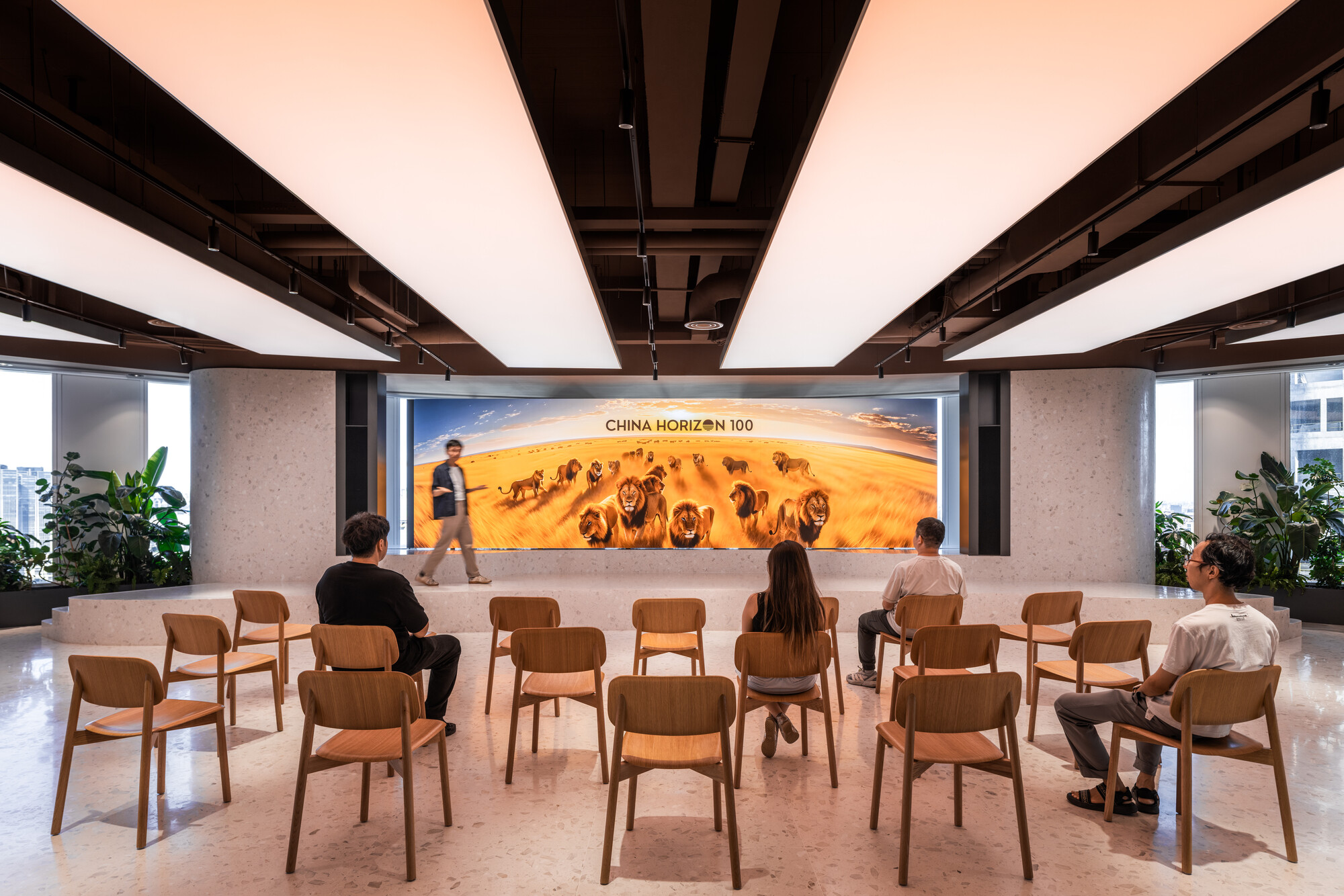 Wooden chairs arranged in rows facing a large illuminated photographic mural with people seated