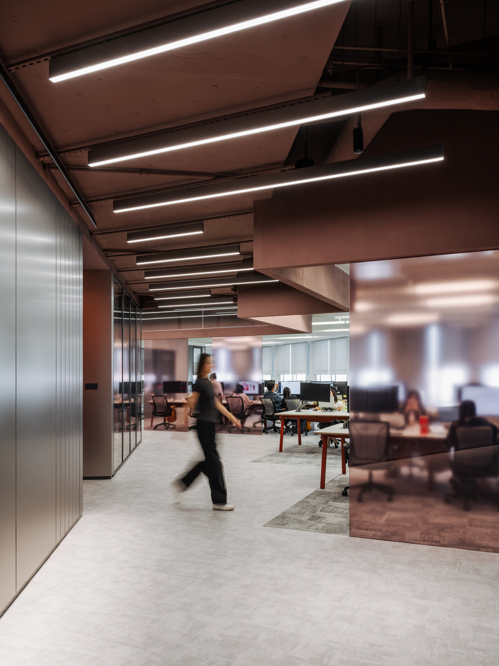 Open-plan workspace with glass partitions and a person walking through in motion blur