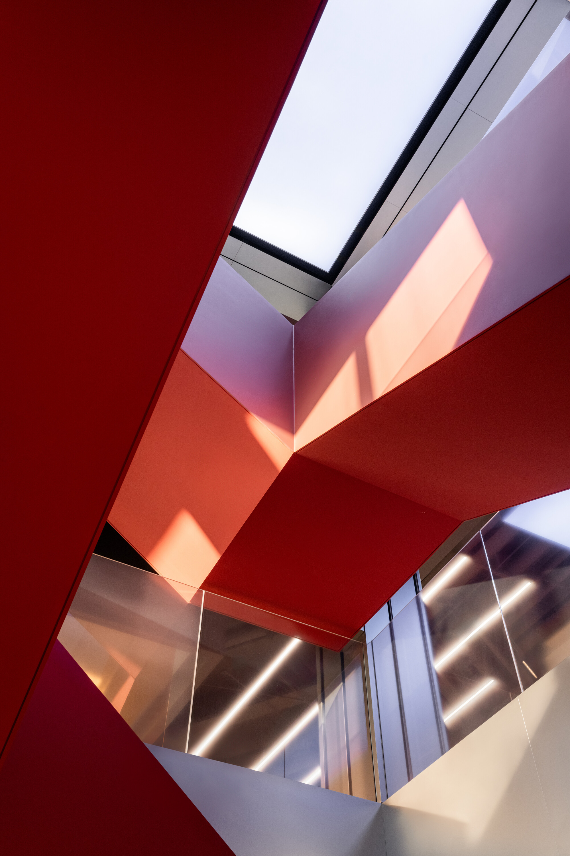 Upward view of a multi-story atrium with red-painted angular ceiling planes and a skylight above