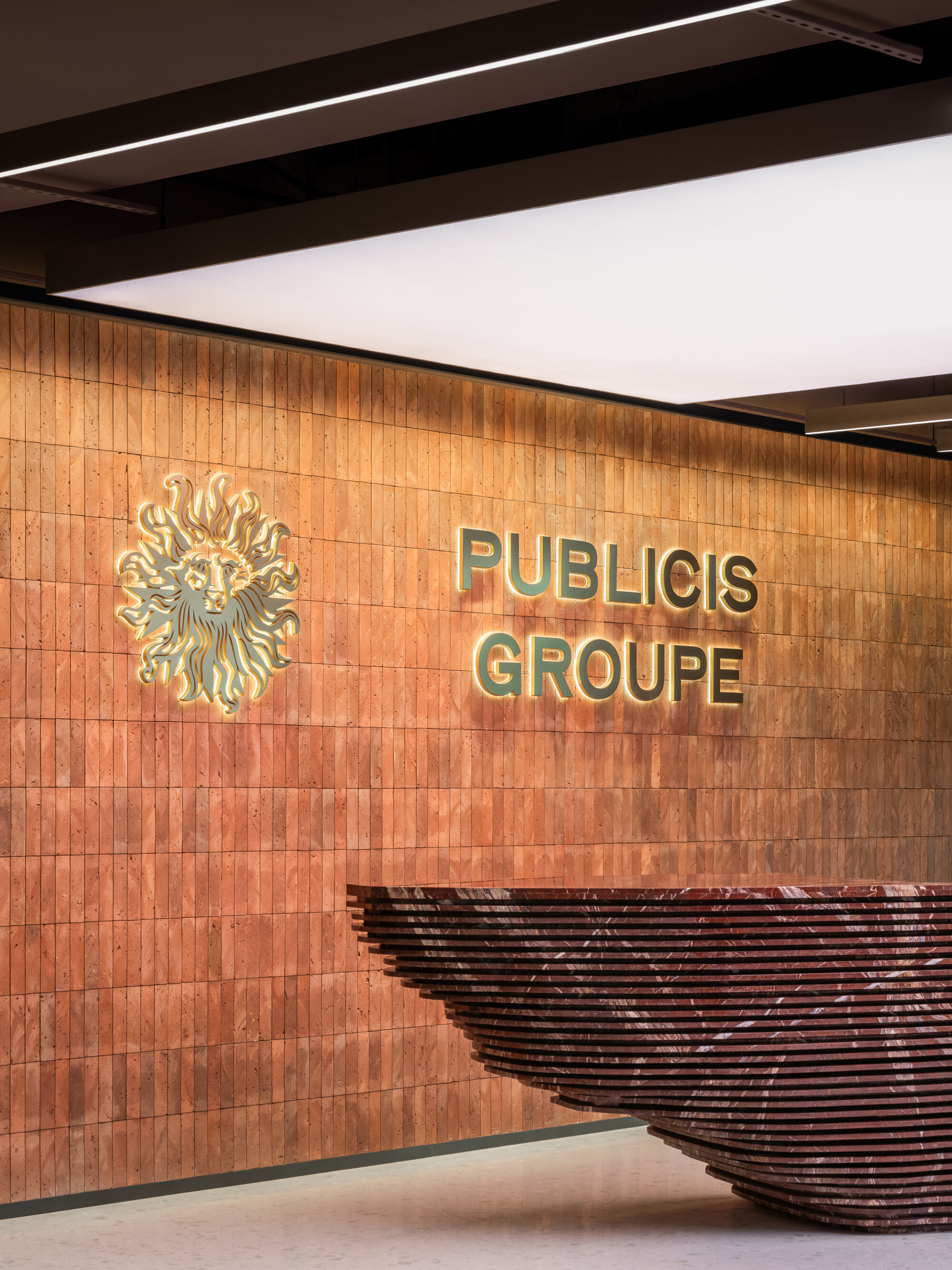 Timber-clad reception wall with brass lettering and a sculptural woven reception desk under linear ceiling lighting