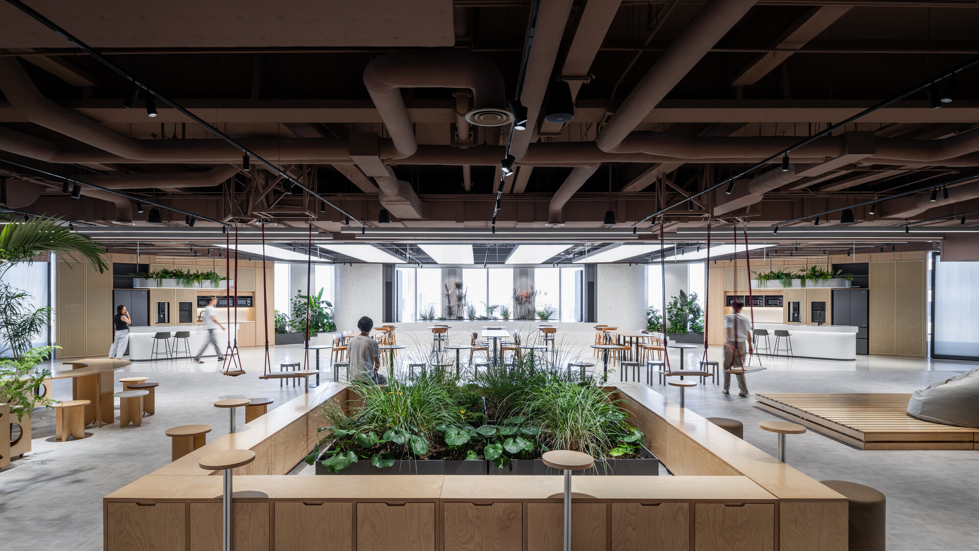 Communal workspace with raised timber planters, high tables and people gathering under an exposed ceiling structure