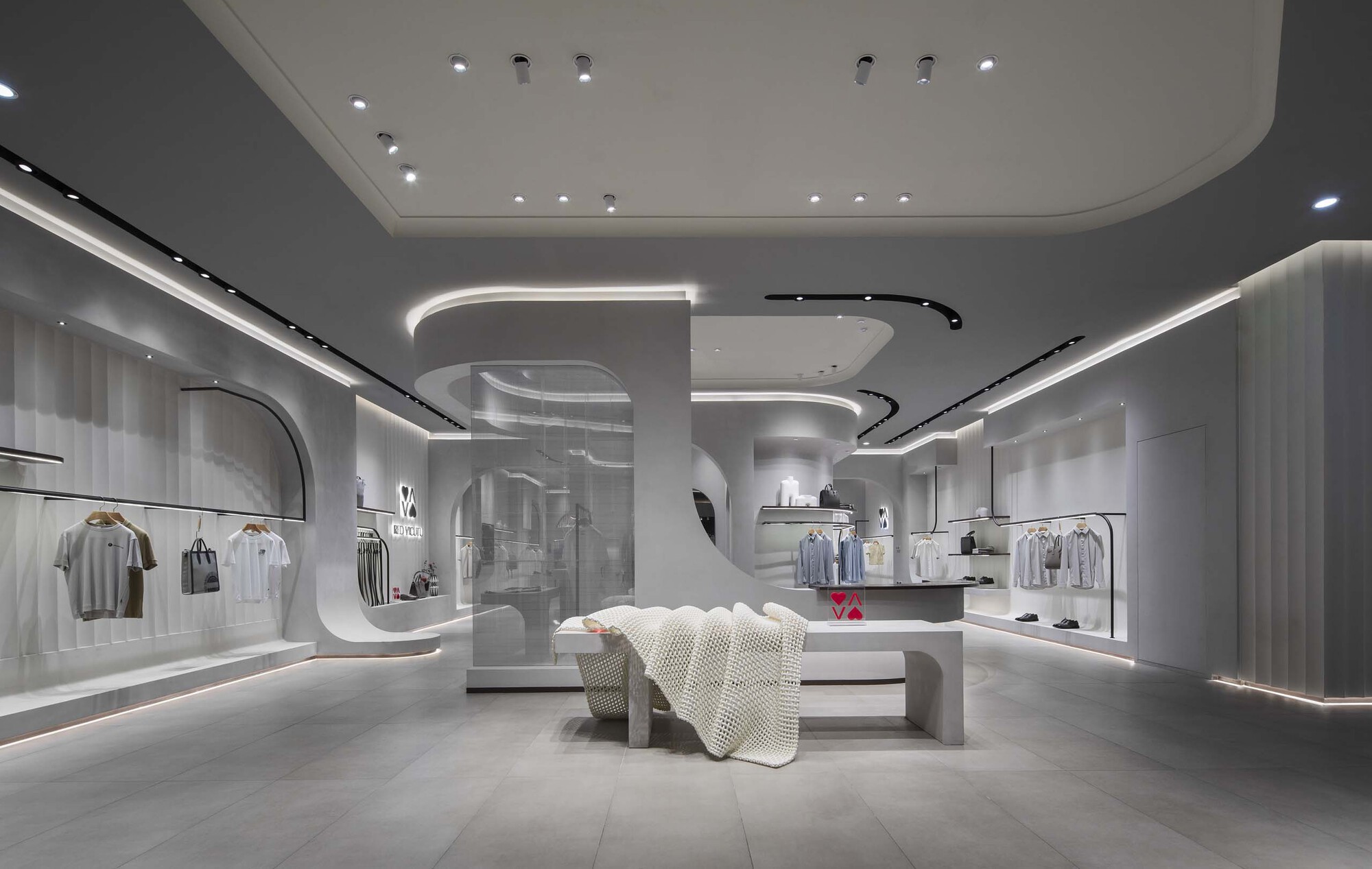 Interior of a retail space with curved white ceiling elements, recessed linear lighting, and central display table