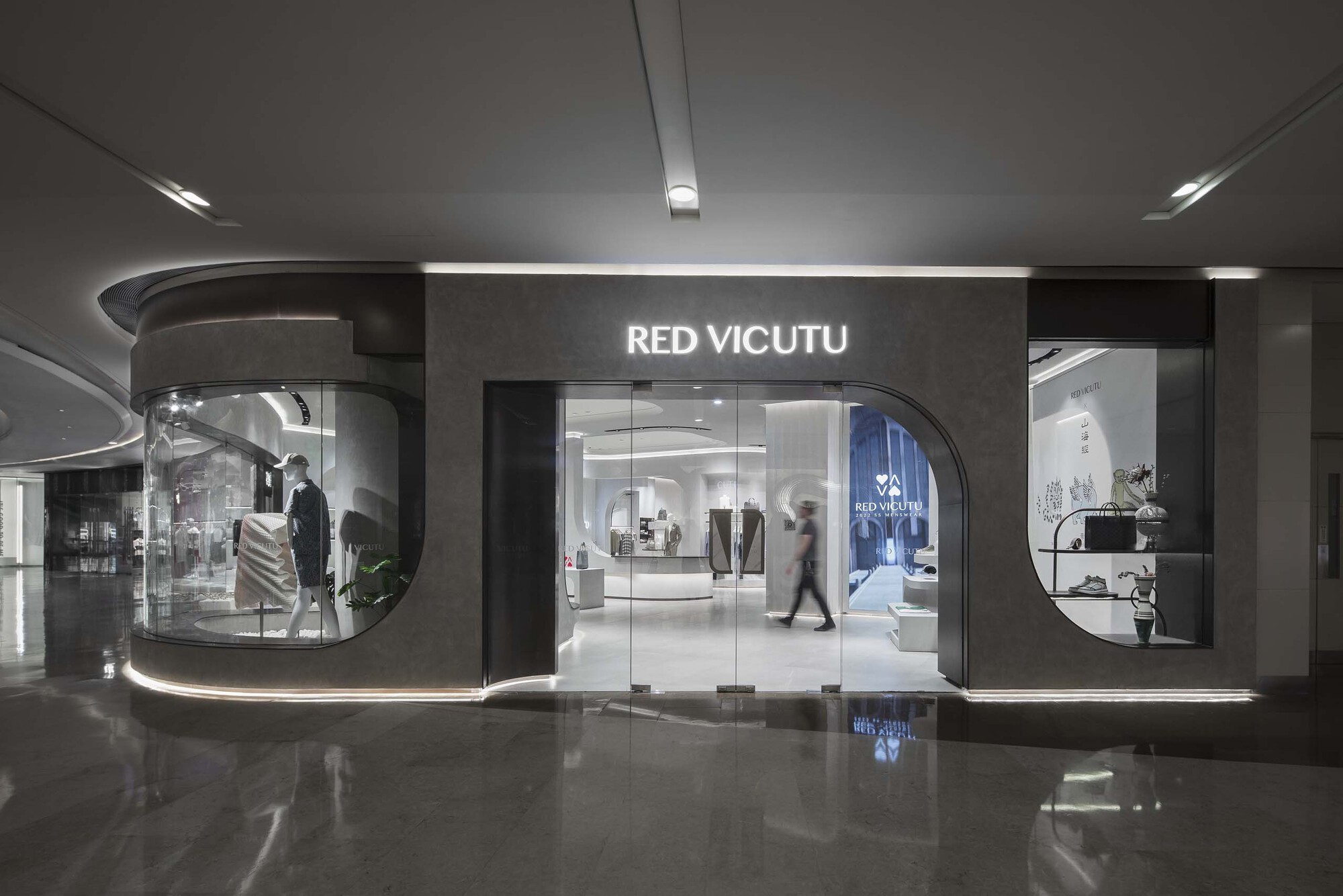 Glass storefront with curved vitrine and polished dark floor reflecting the illuminated display windows