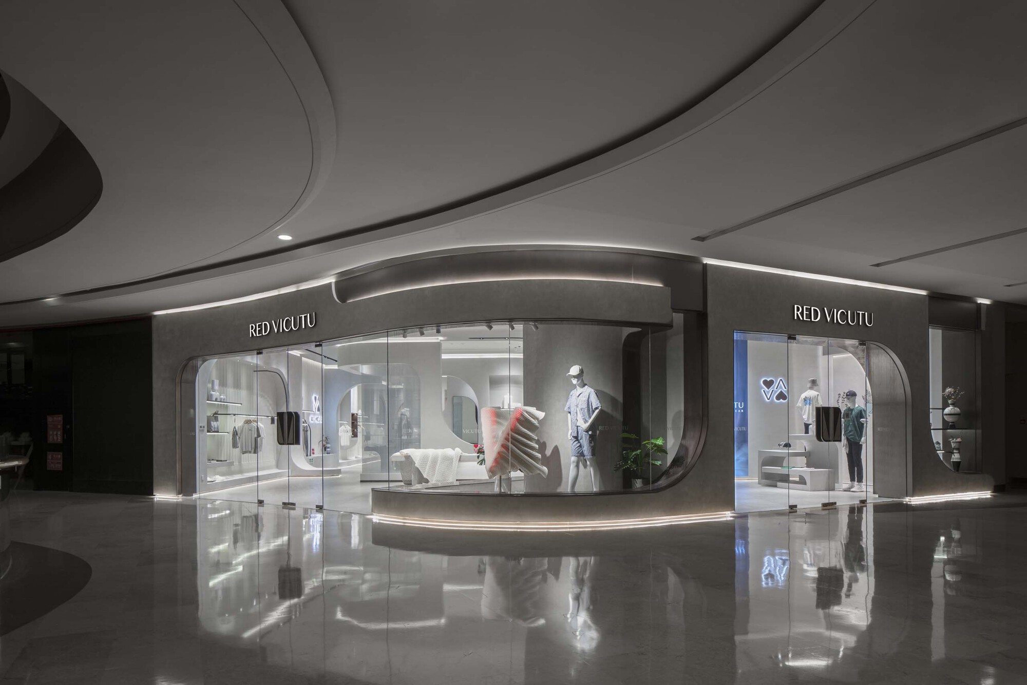 Storefront facade with curved glass and gray stone surround reflected in the glossy mall floor