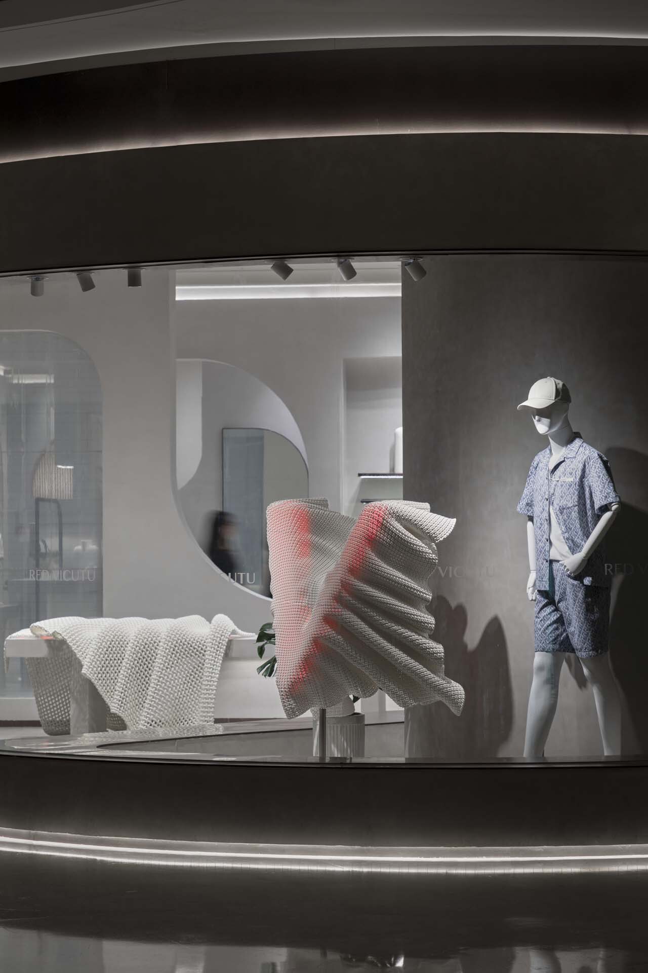 Display window with mannequin and textured sculptural element behind curved glass