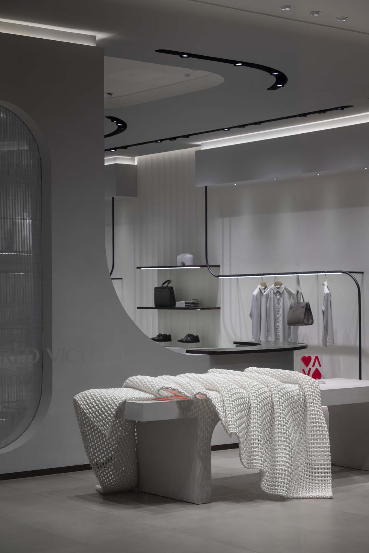 Display area with black curved ceiling track, glass shelving and upholstered seating in foreground