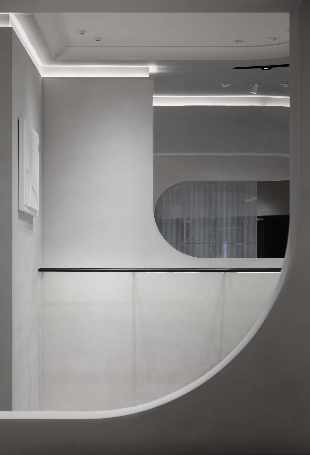 Curved white reception desk with black metal rail beneath horizontal strip lighting