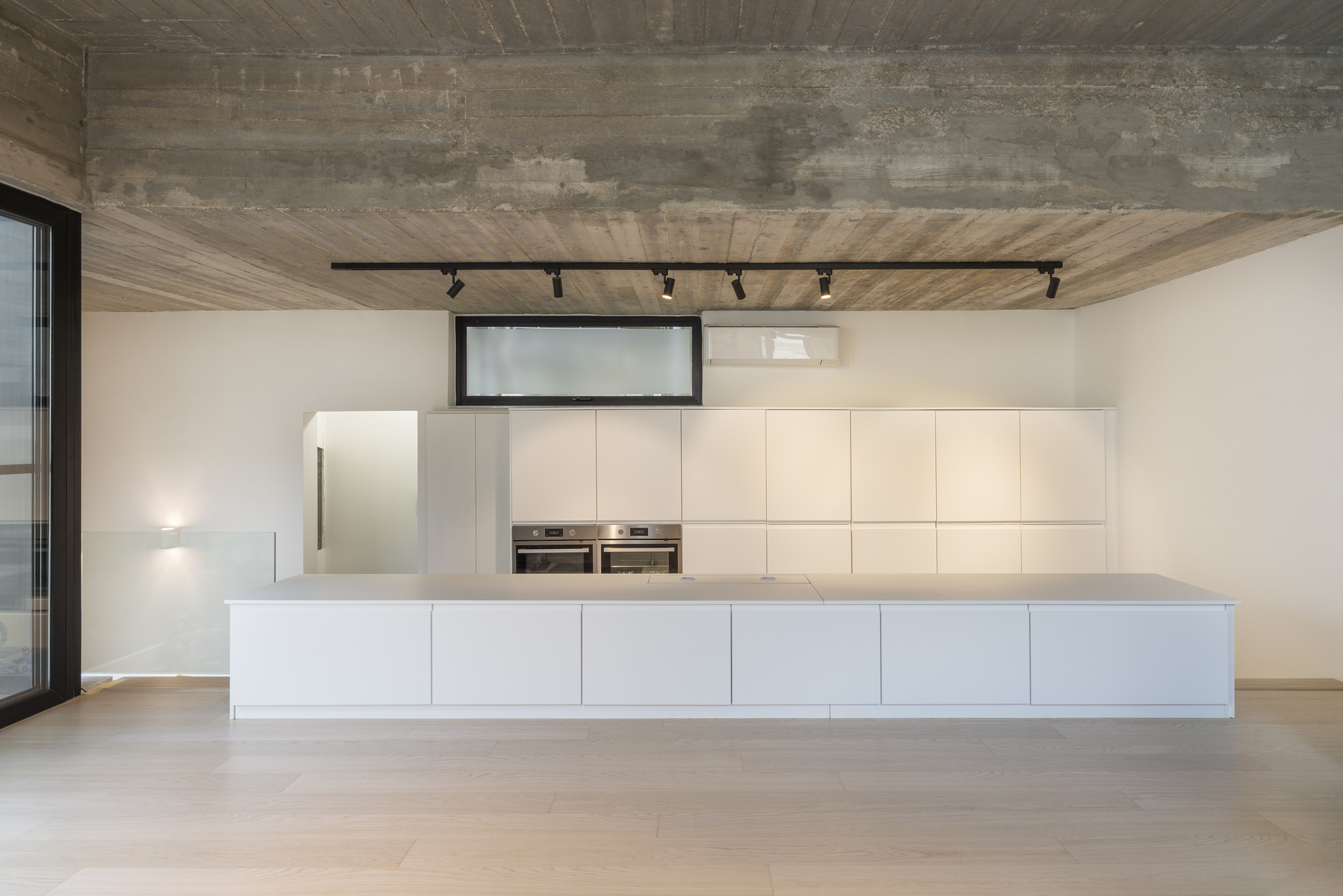 Kitchen with white island and wall cabinetry below board-formed concrete ceiling and black track lighting