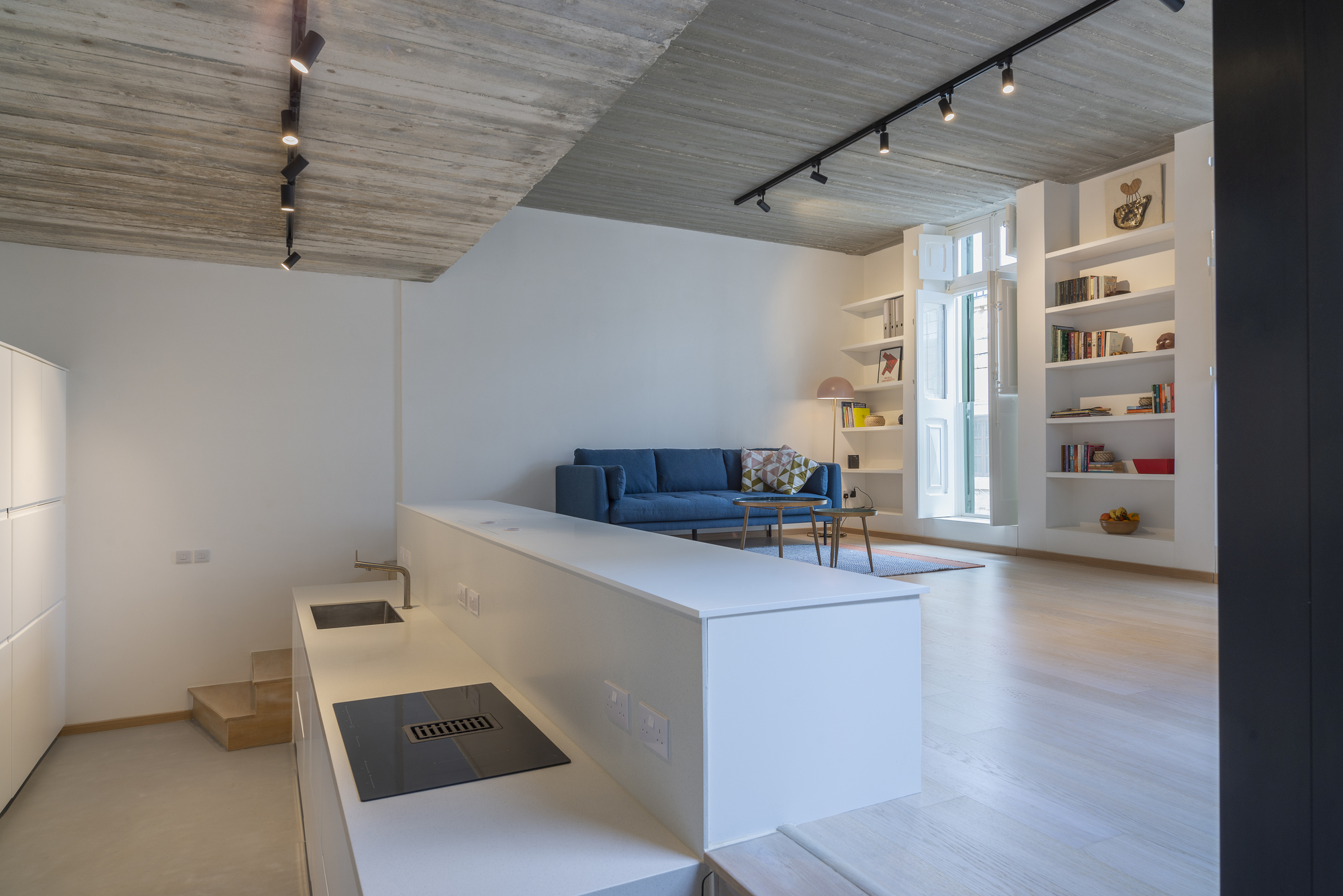 Open-plan living area with blue sofa, built-in shelving, and board-formed concrete ceiling under track lighting