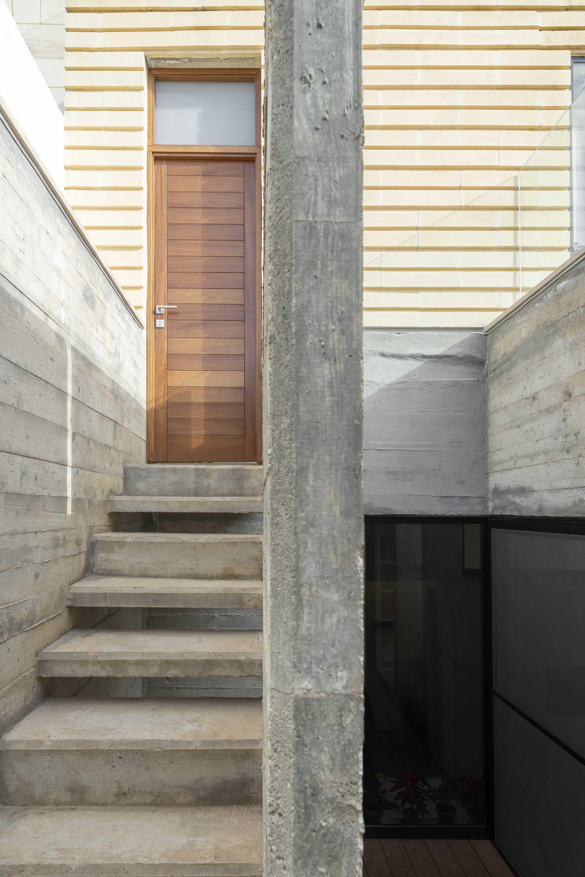 Concrete stairs leading up to a wooden door flanked by board-formed concrete walls and a weathered column