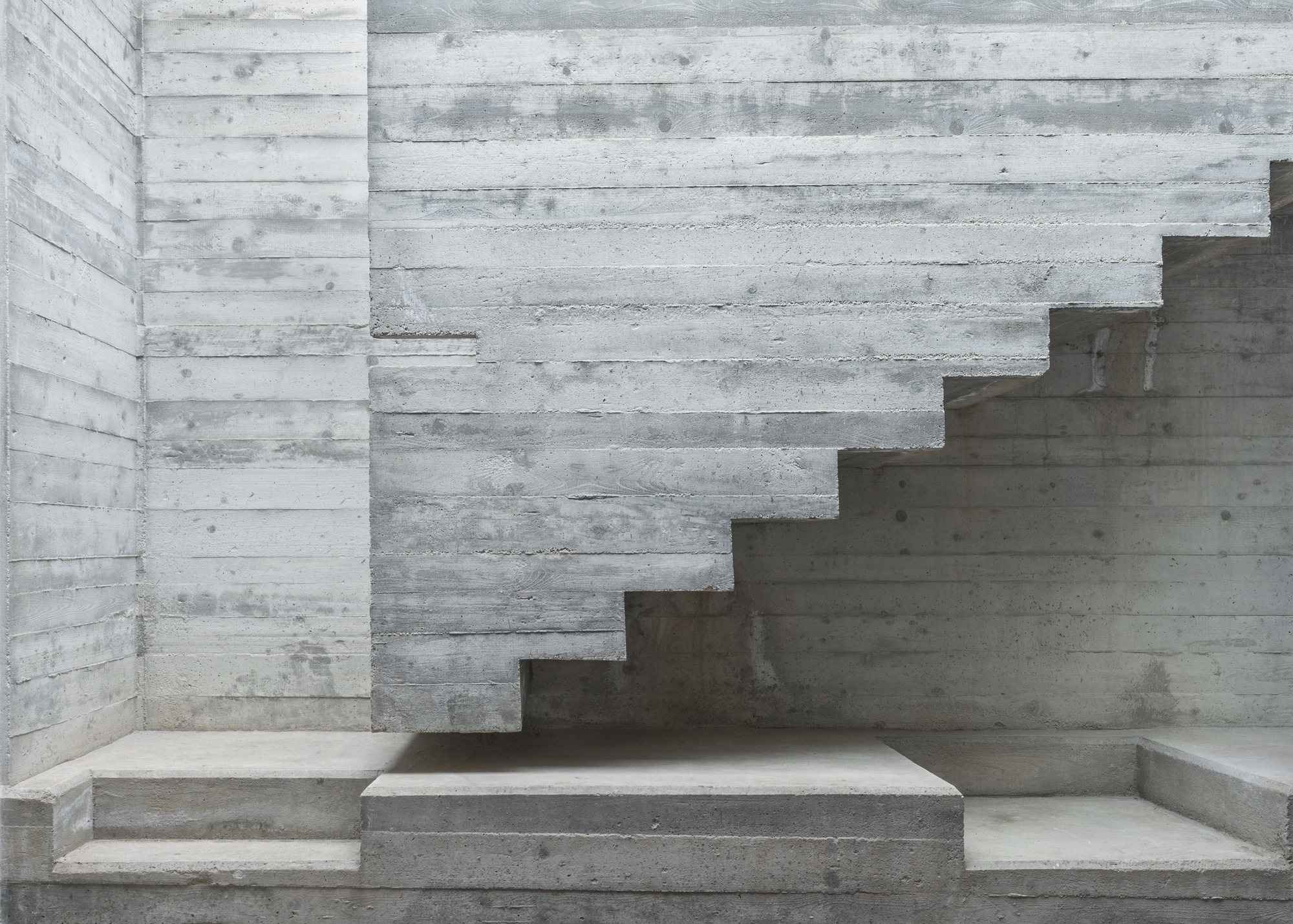 Intersecting concrete stair volumes with board-formed texture and varied tread depths at multiple levels