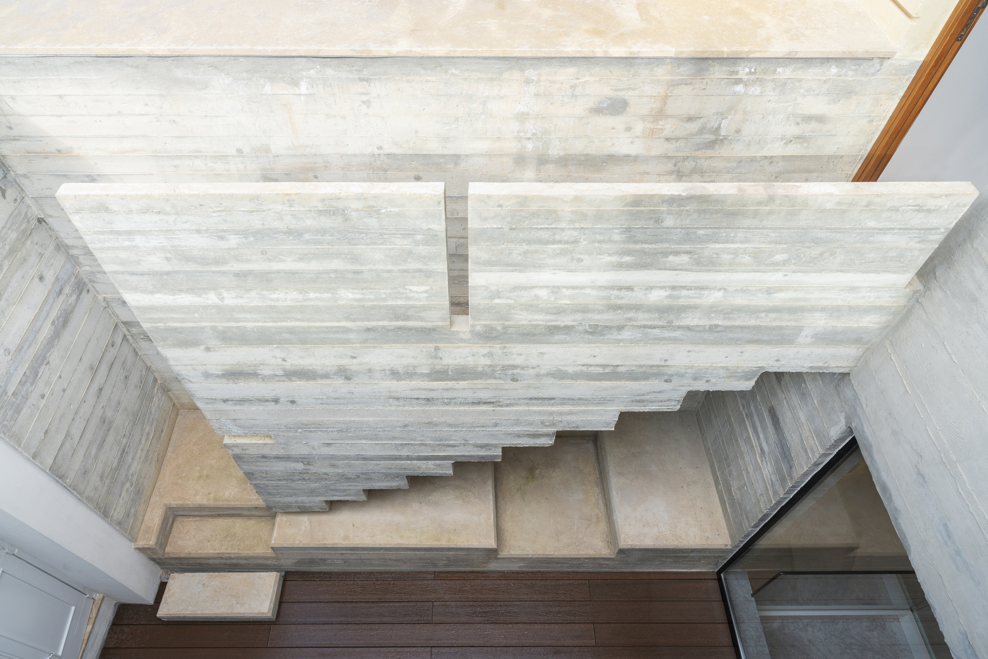 Overhead view of concrete stairs beneath a board-formed ceiling with natural light filtering through
