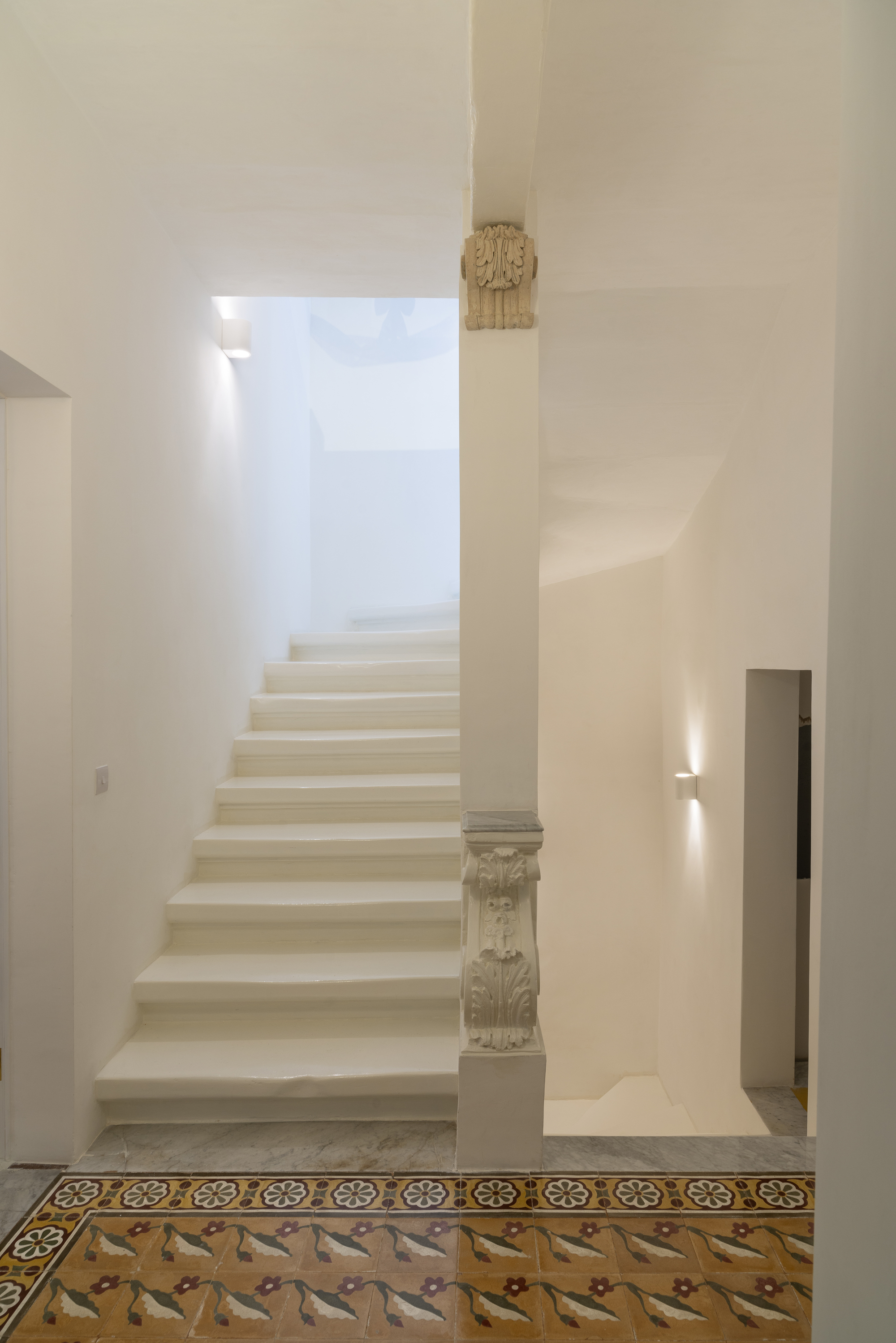 White plastered staircase with carved stone balustrade above decorative patterned floor tiles