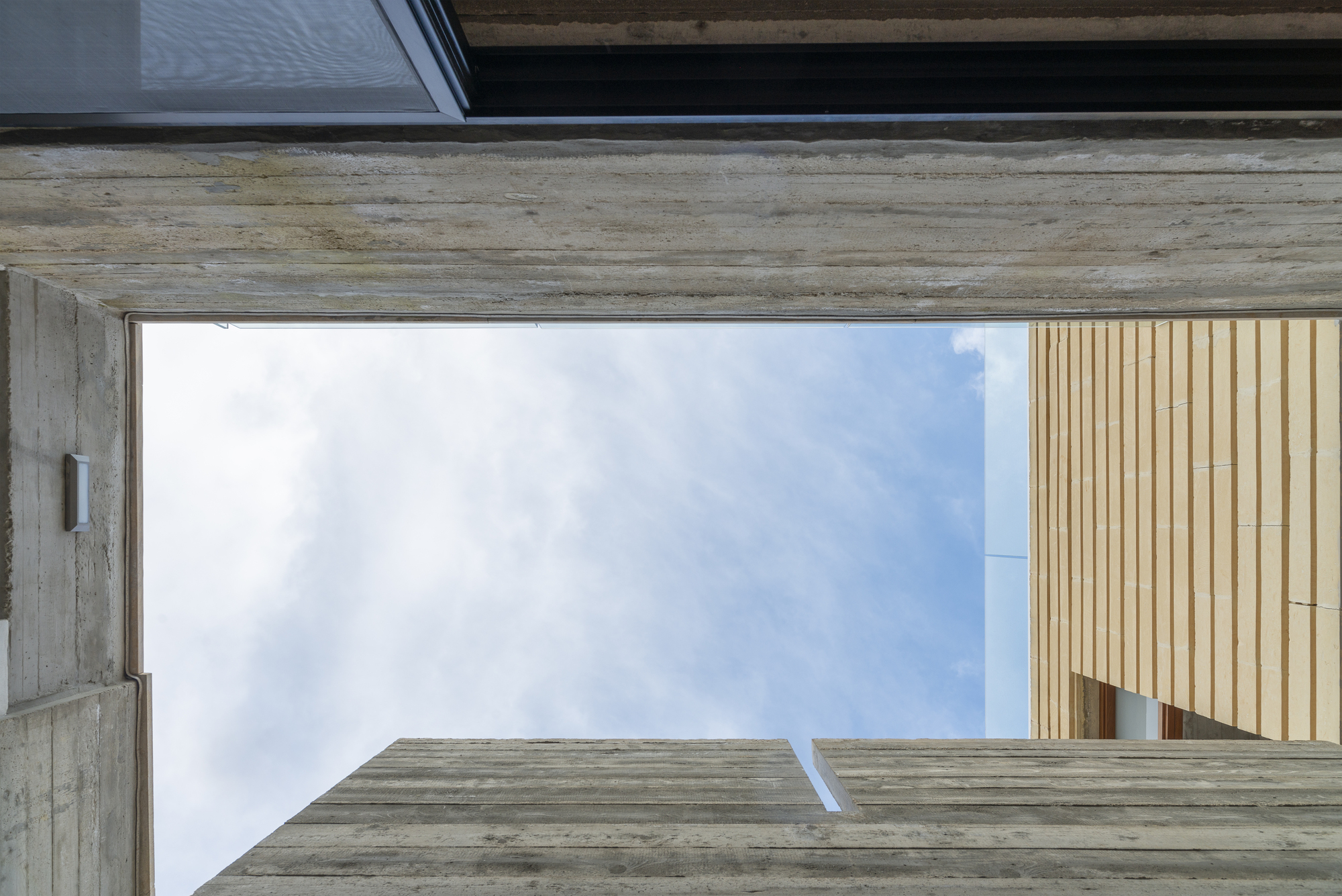 Upward view framed by board-formed concrete beams with timber cladding against the sky