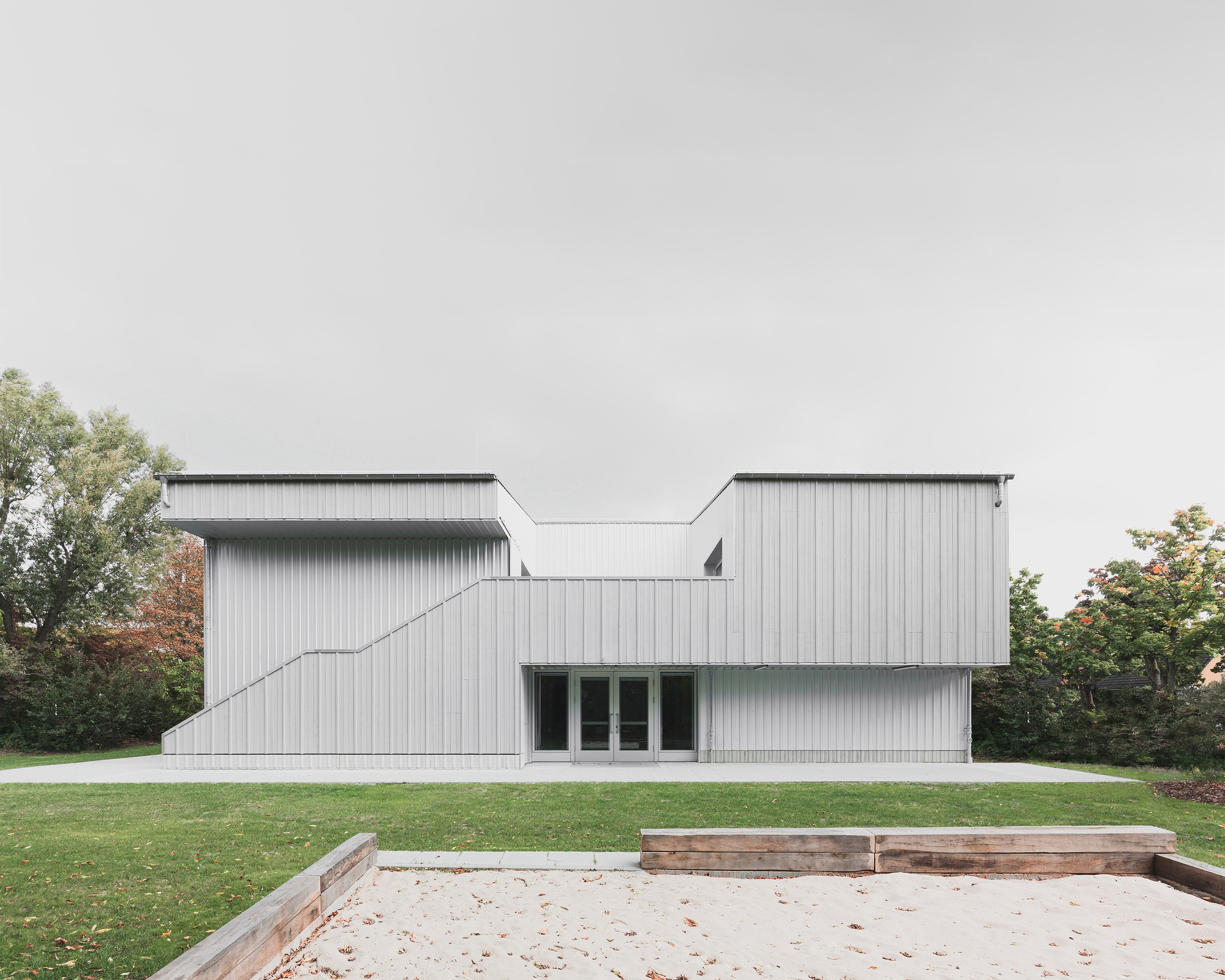 Garden elevation of the corrugated metal facade with stepped volumes behind a timber-edged sandbox