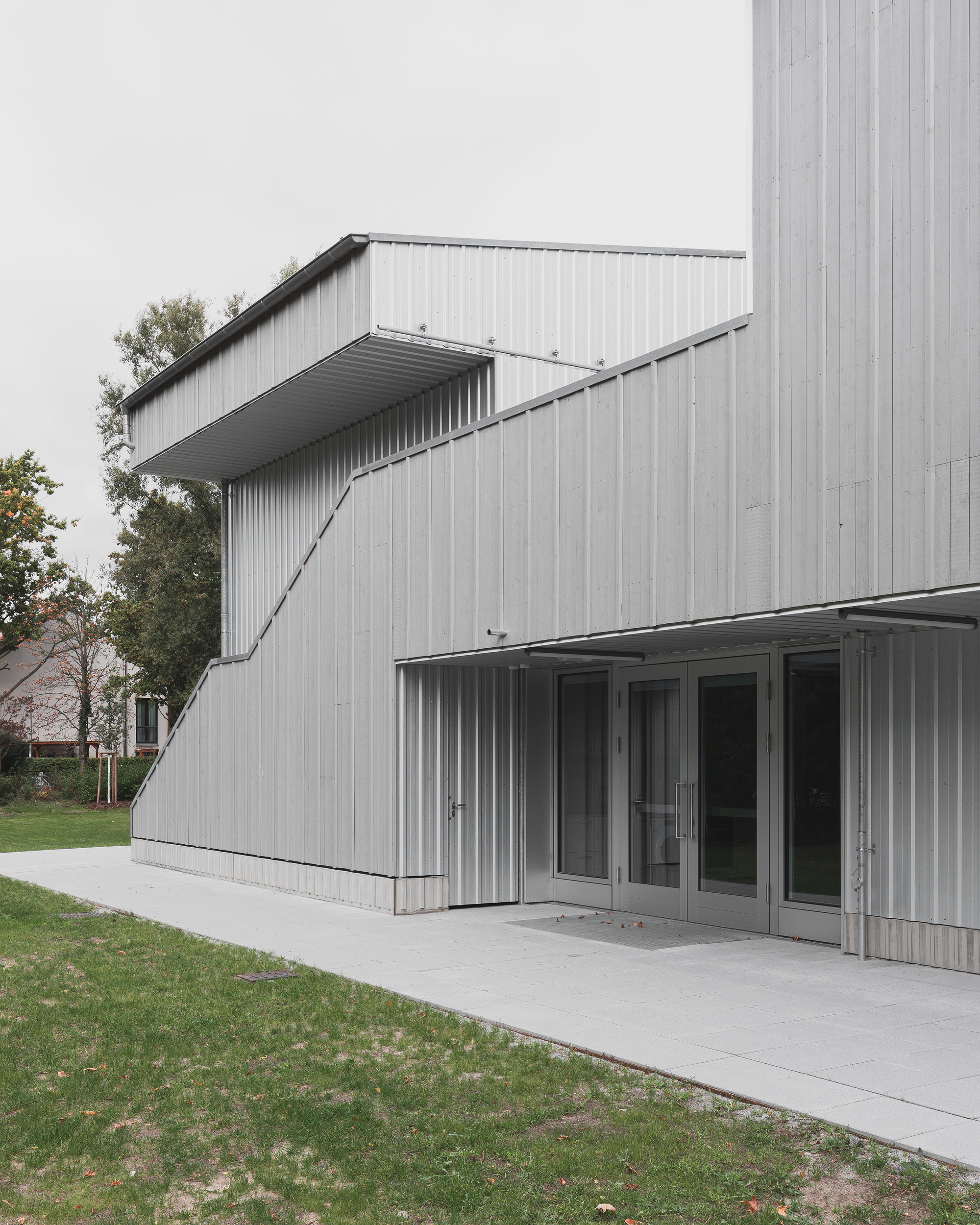 Angled canopy projection above glass doors and concrete terrace on corrugated metal volume