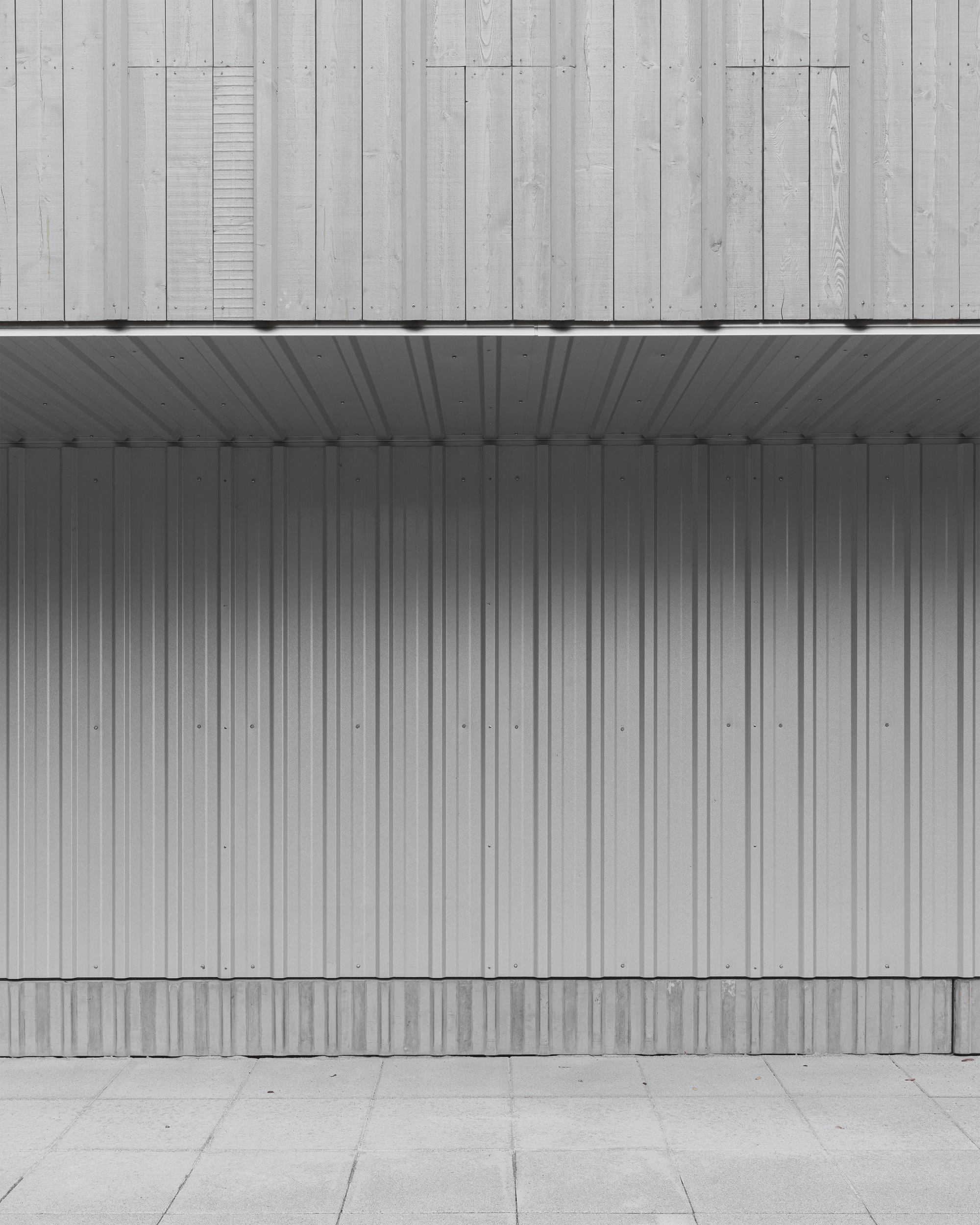 Covered entry with vertical metal cladding and weathered timber facade above a concrete paver courtyard