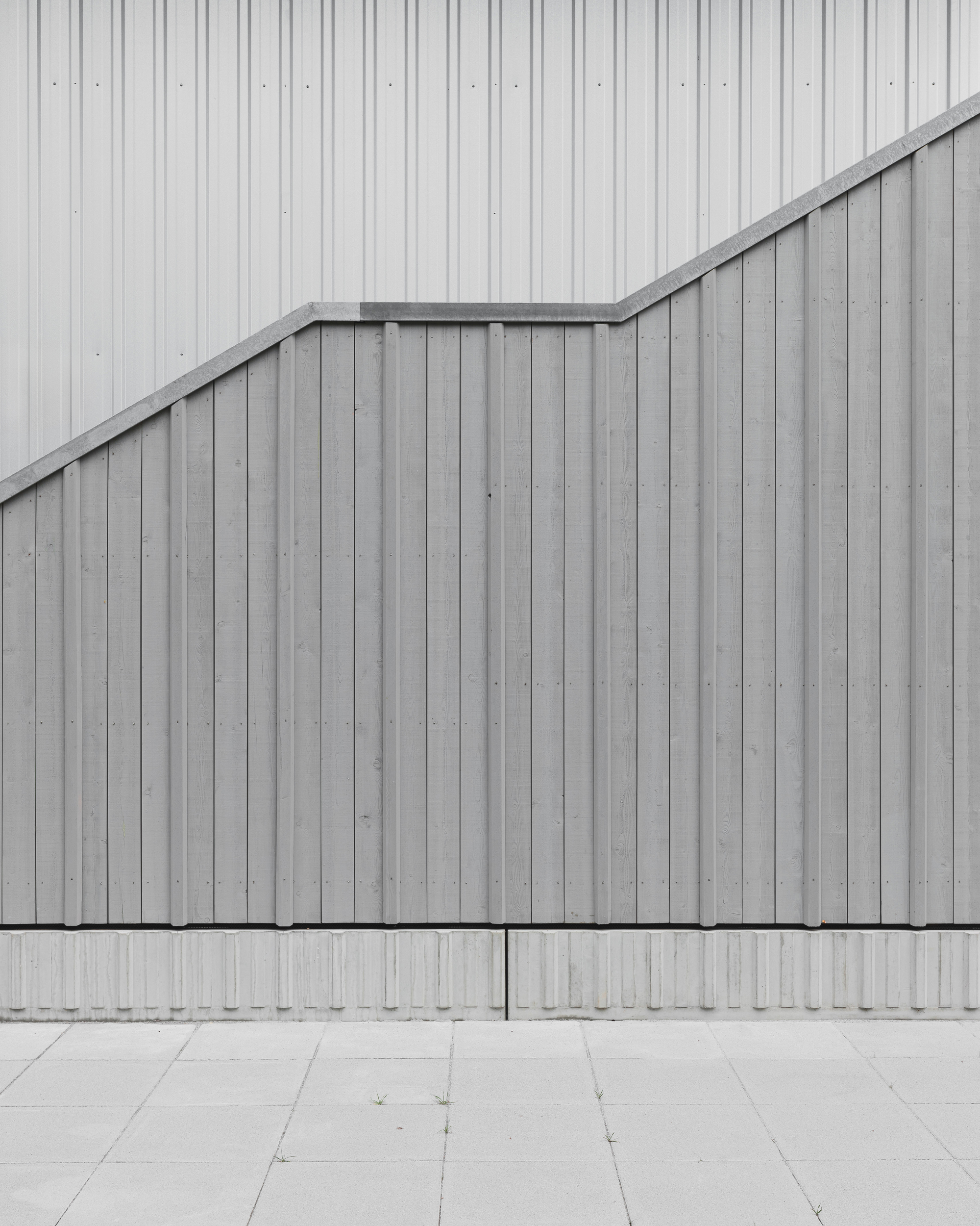Exterior detail of vertical metal panel facade with angular roofline meeting concrete pavers