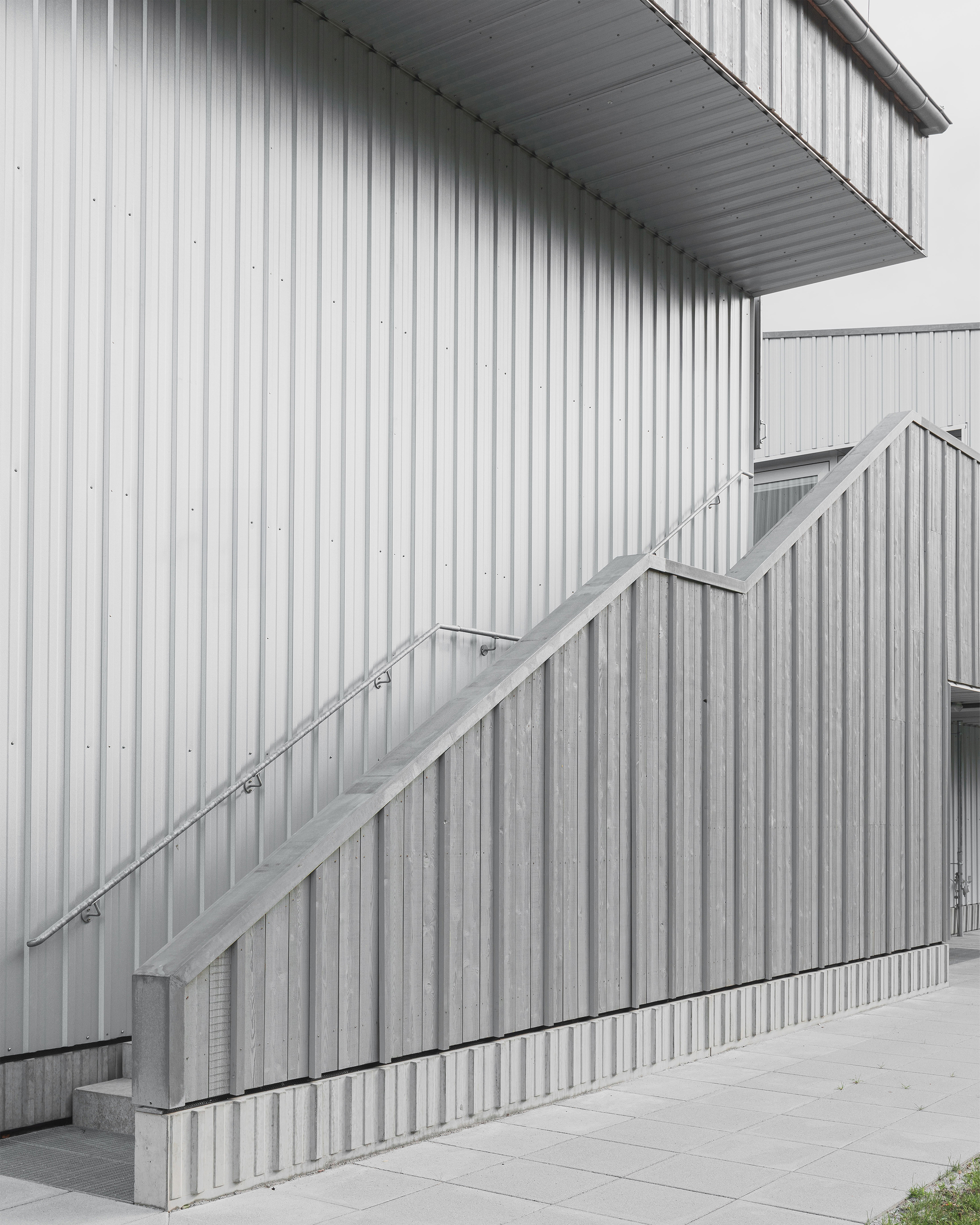 Exterior staircase with metal handrail ascending corrugated metal panel cladding on an overcast day