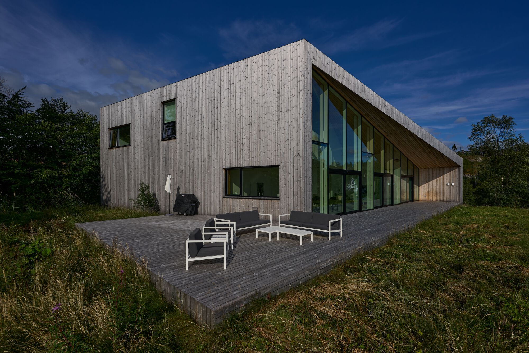 Vertical wood-clad facade with scattered windows and a cantilevered timber deck at dusk