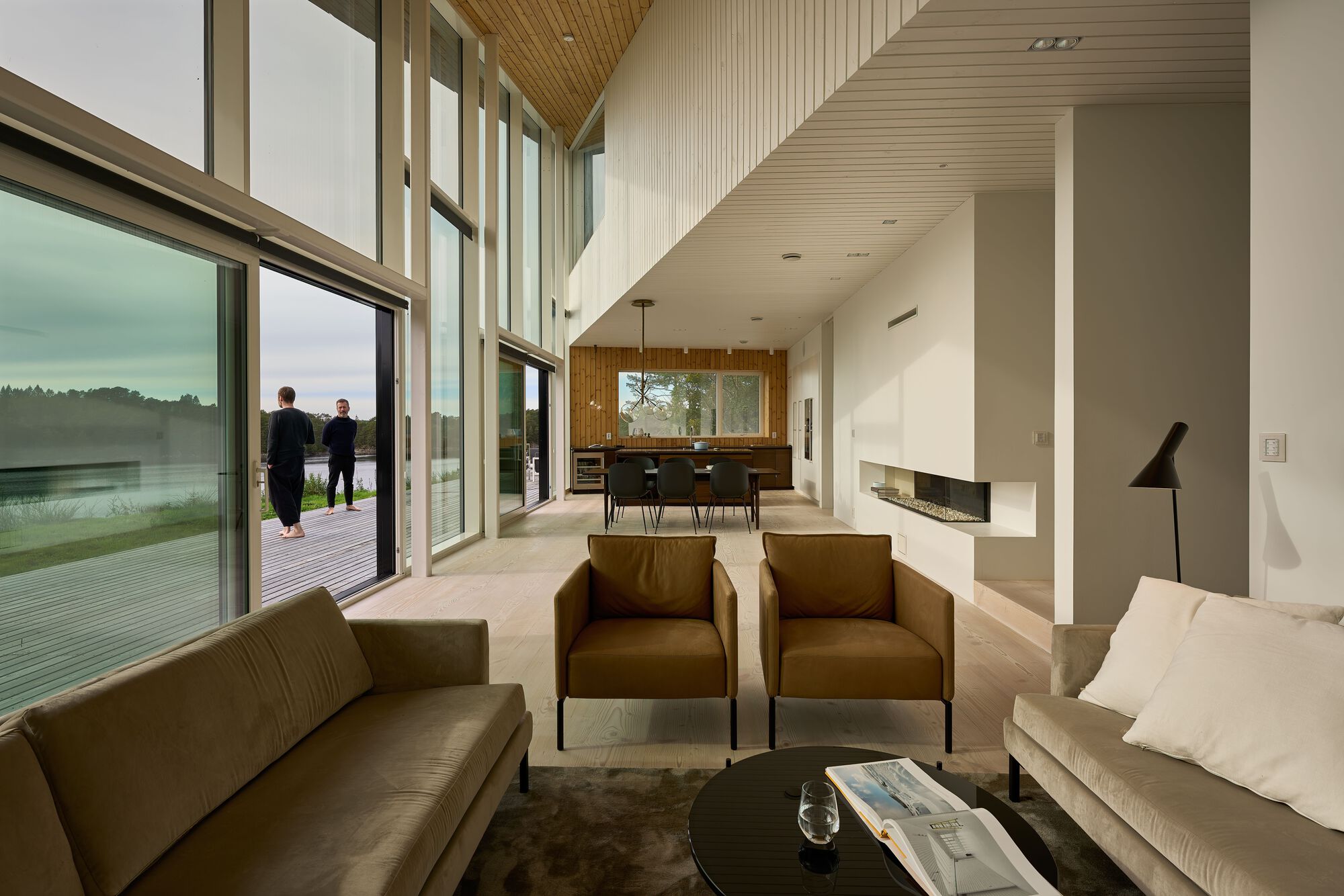 Open living space with timber ceiling and floor-to-ceiling glazing overlooking two figures on the terrace
