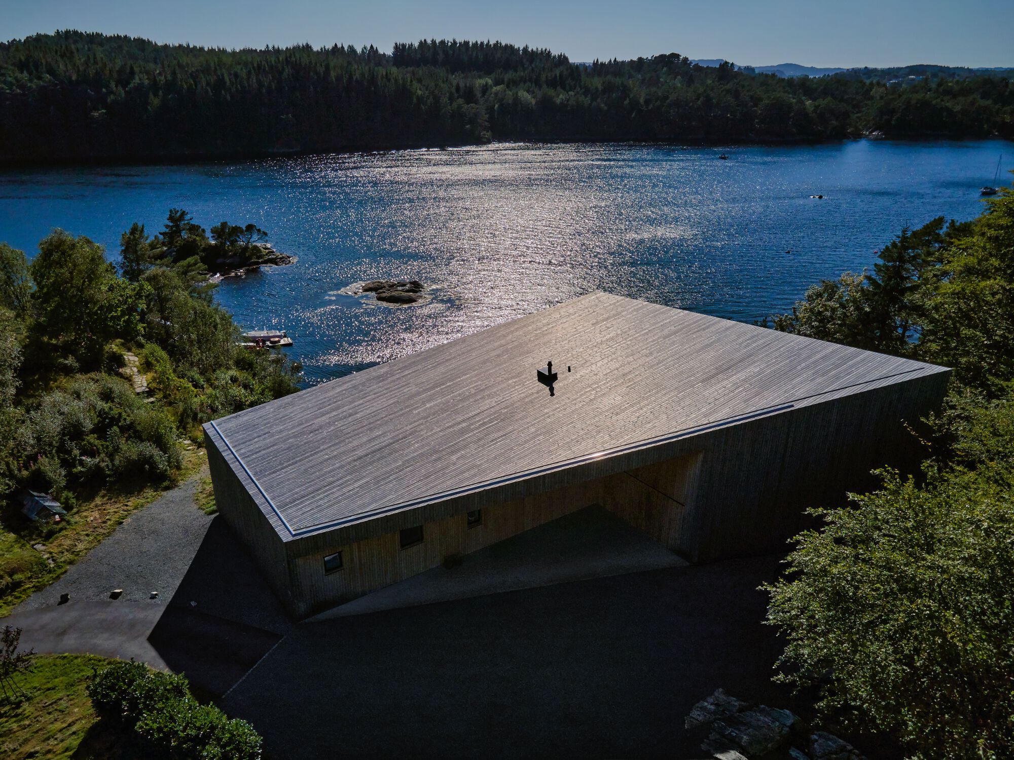 Aerial view of the low-pitched timber roof extending over the structure beside a sunlit fjord