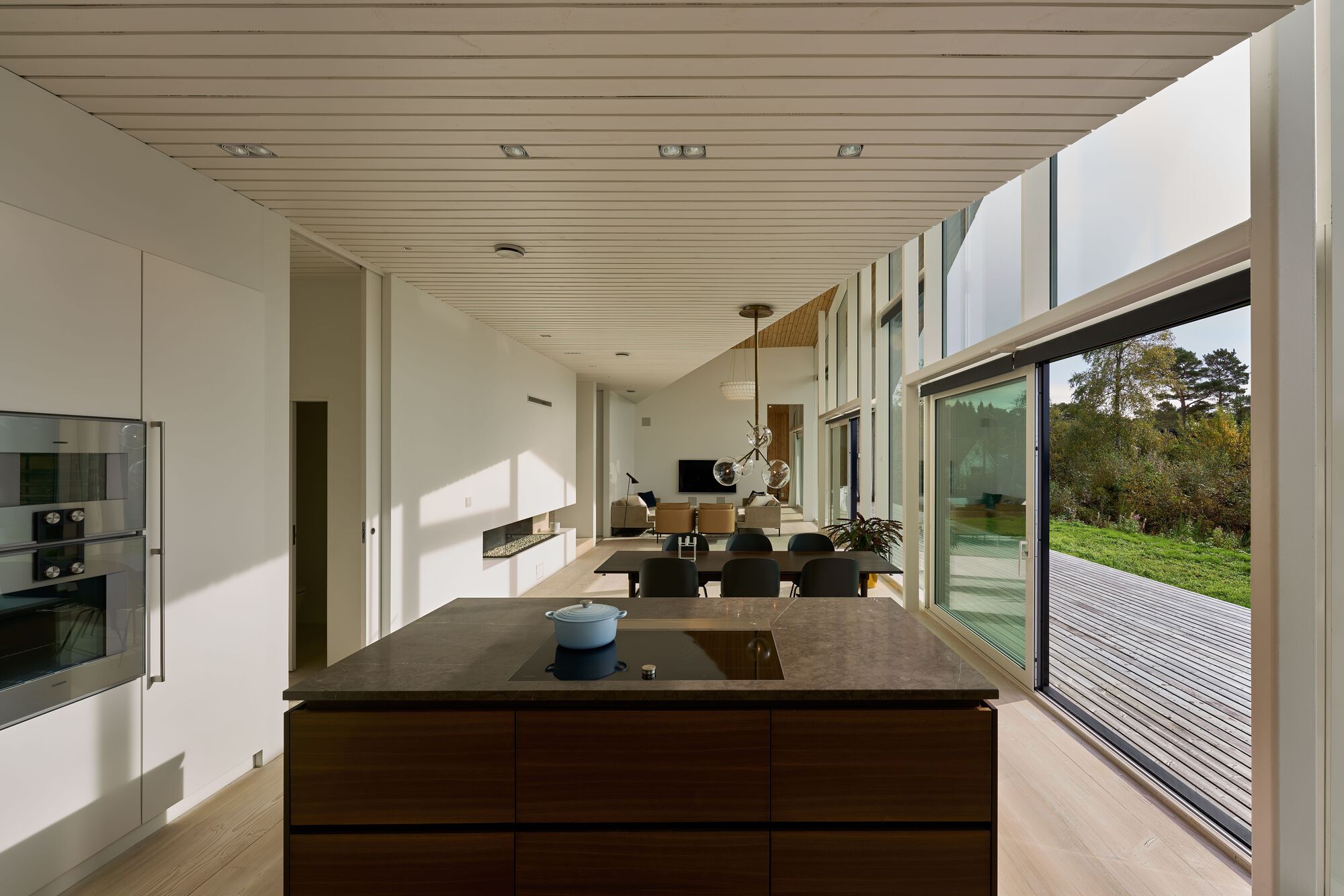 Open-plan living space with timber ceiling and floor-to-ceiling glazing overlooking the terrace