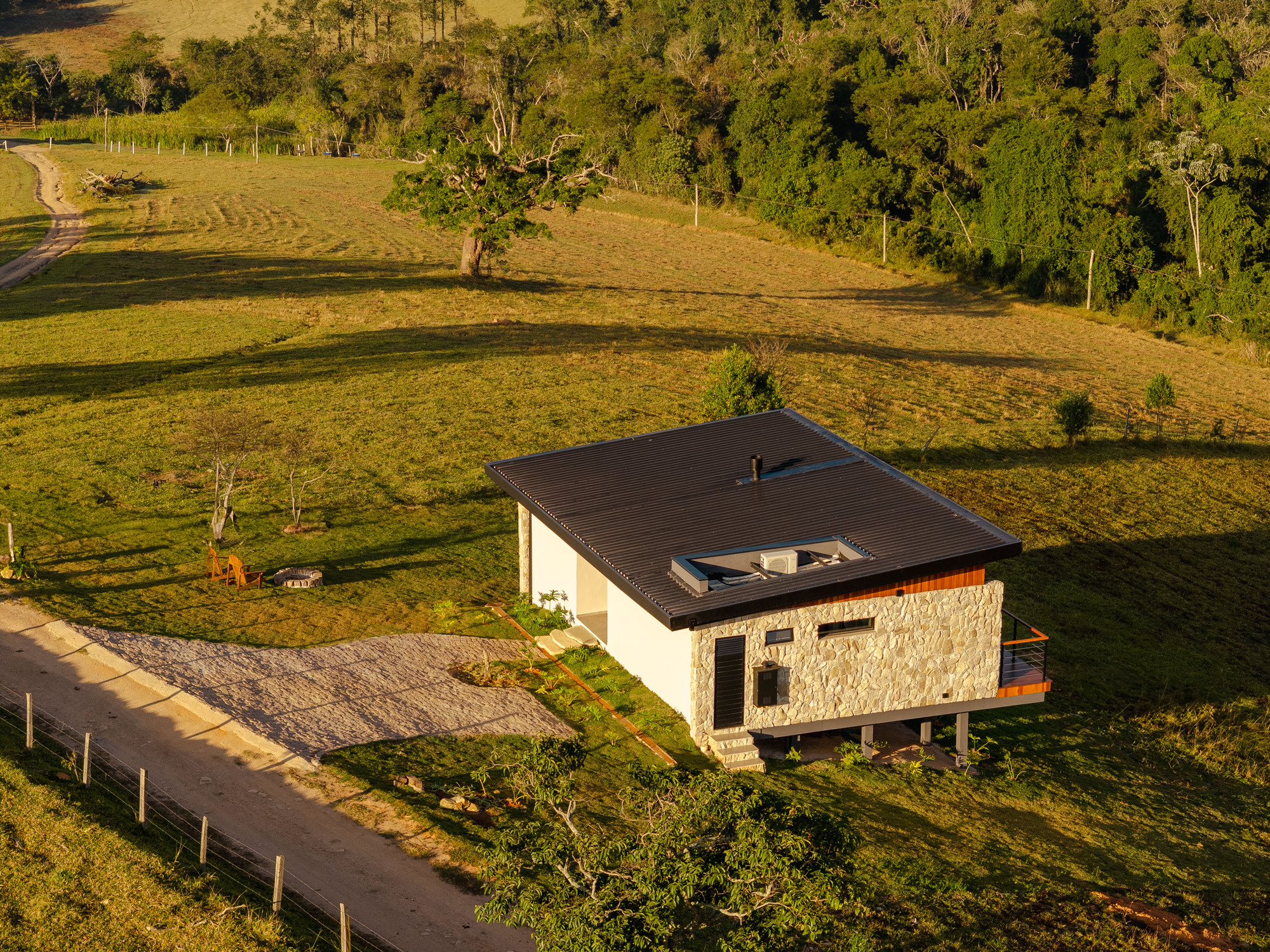 Aerial view of the single-story residence with stone and white plaster walls set in rolling grassland at dusk